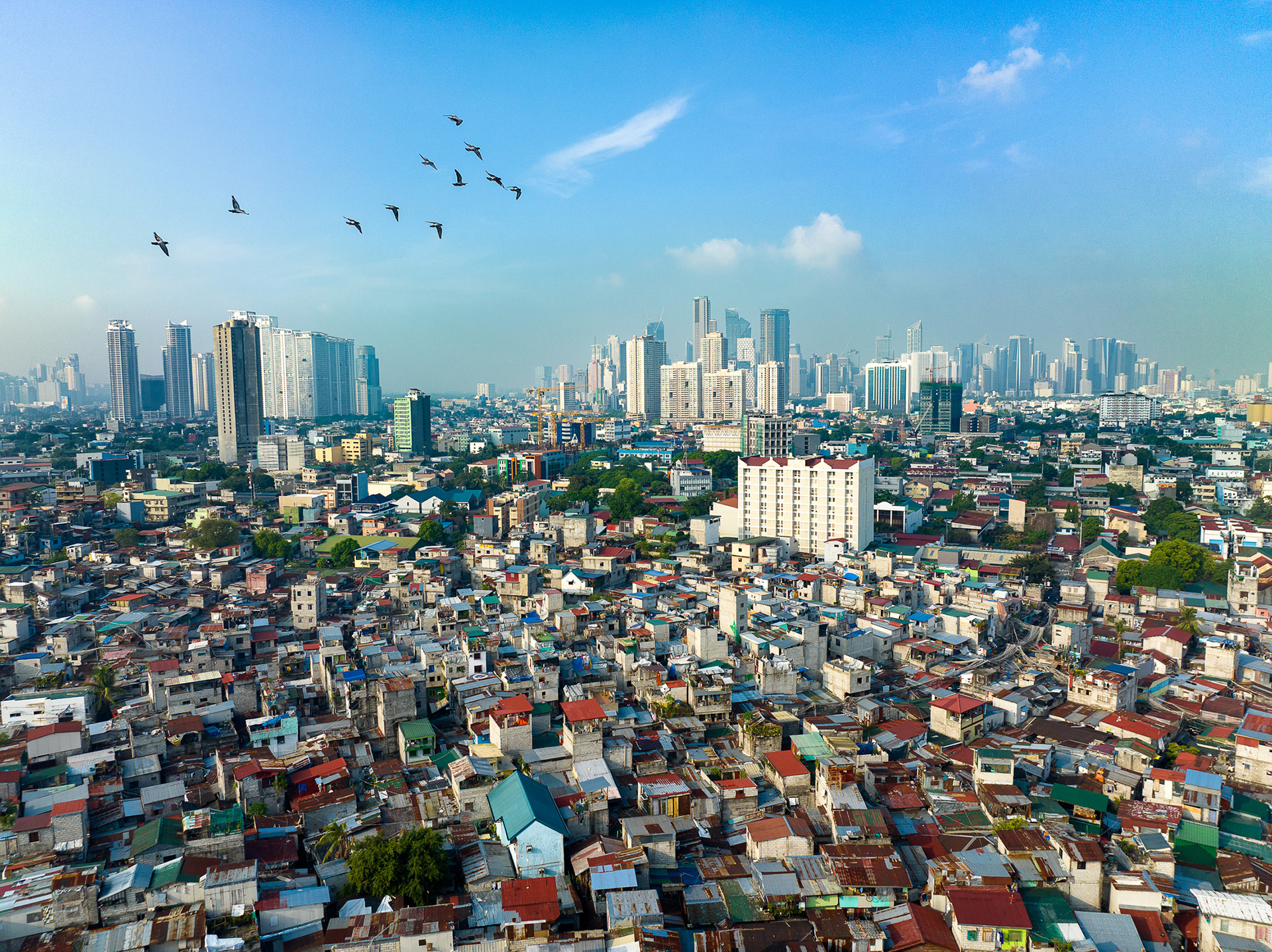 Aerial view of Mandaluyong’s dense housing with Makati skyscrapers in background, showing stark inequality.