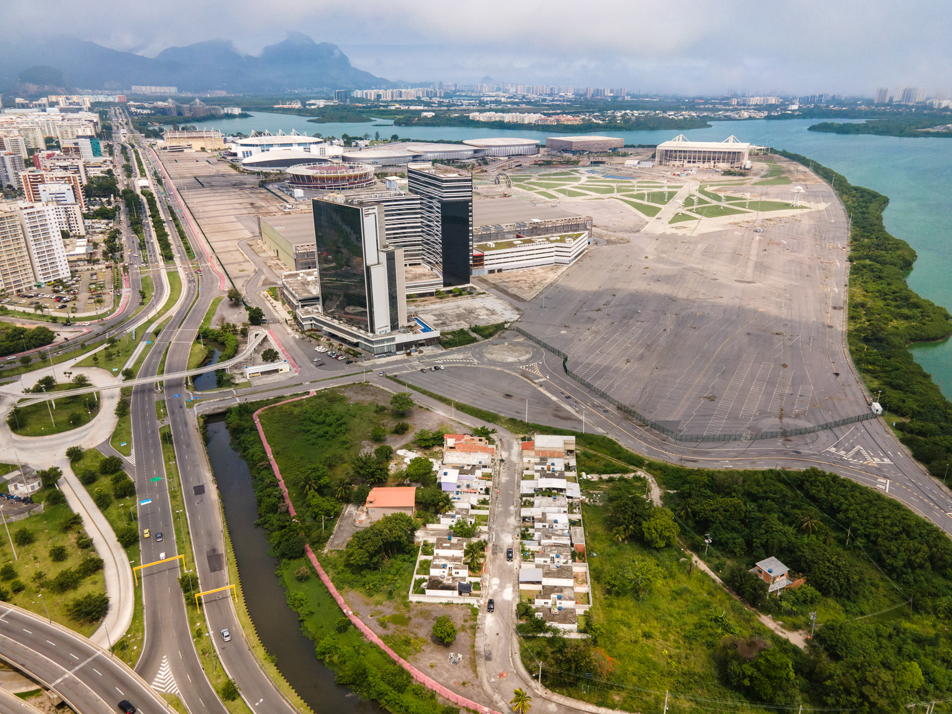 Aerial perspective of Rio’s Olympic redevelopment zone, with Vila Autódromo settlement visible beside wide highways and cleared land.