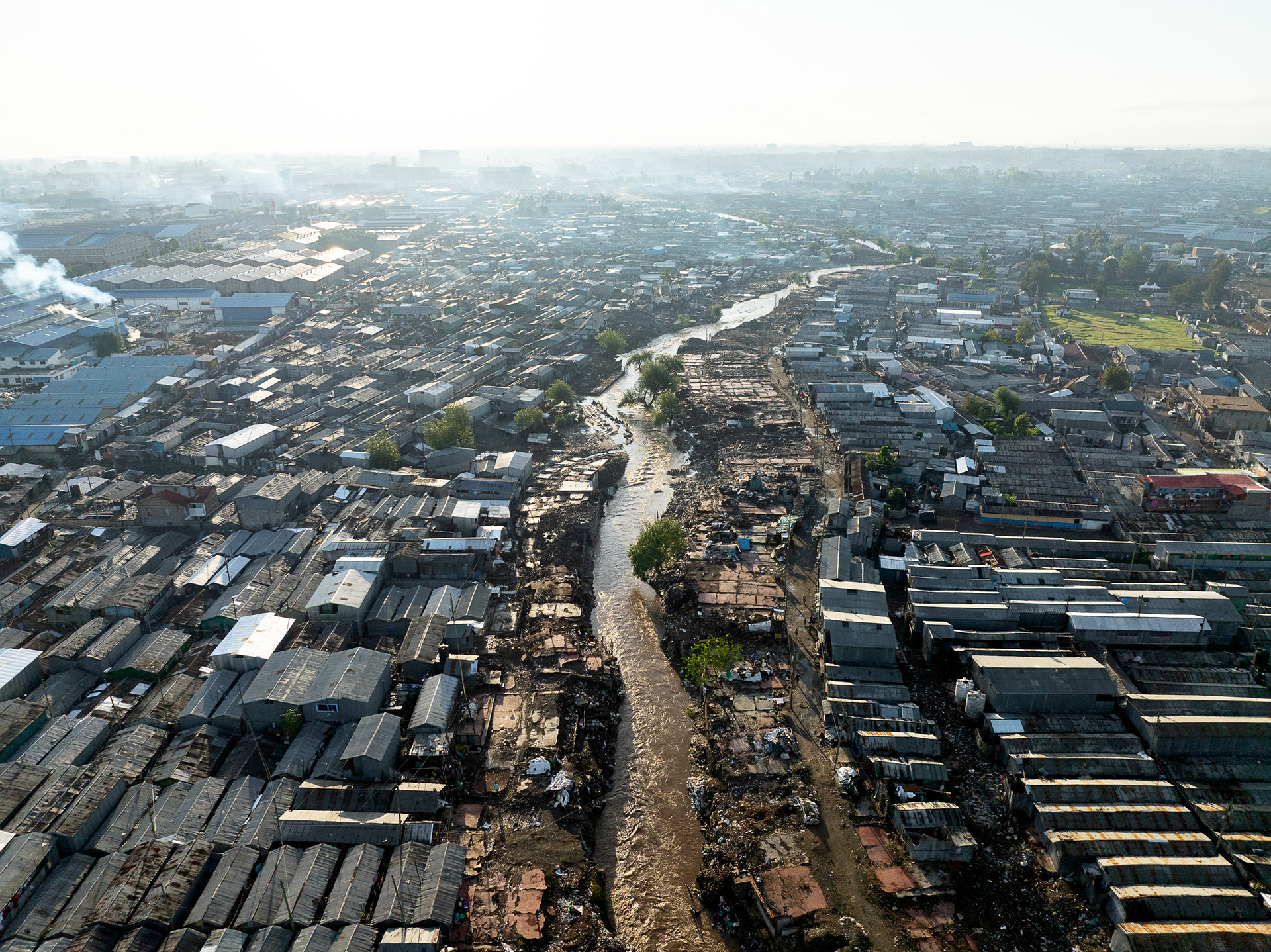 Drone view of river winding through Nairobi’s industrial slum zone, with corrugated buildings on either side.
