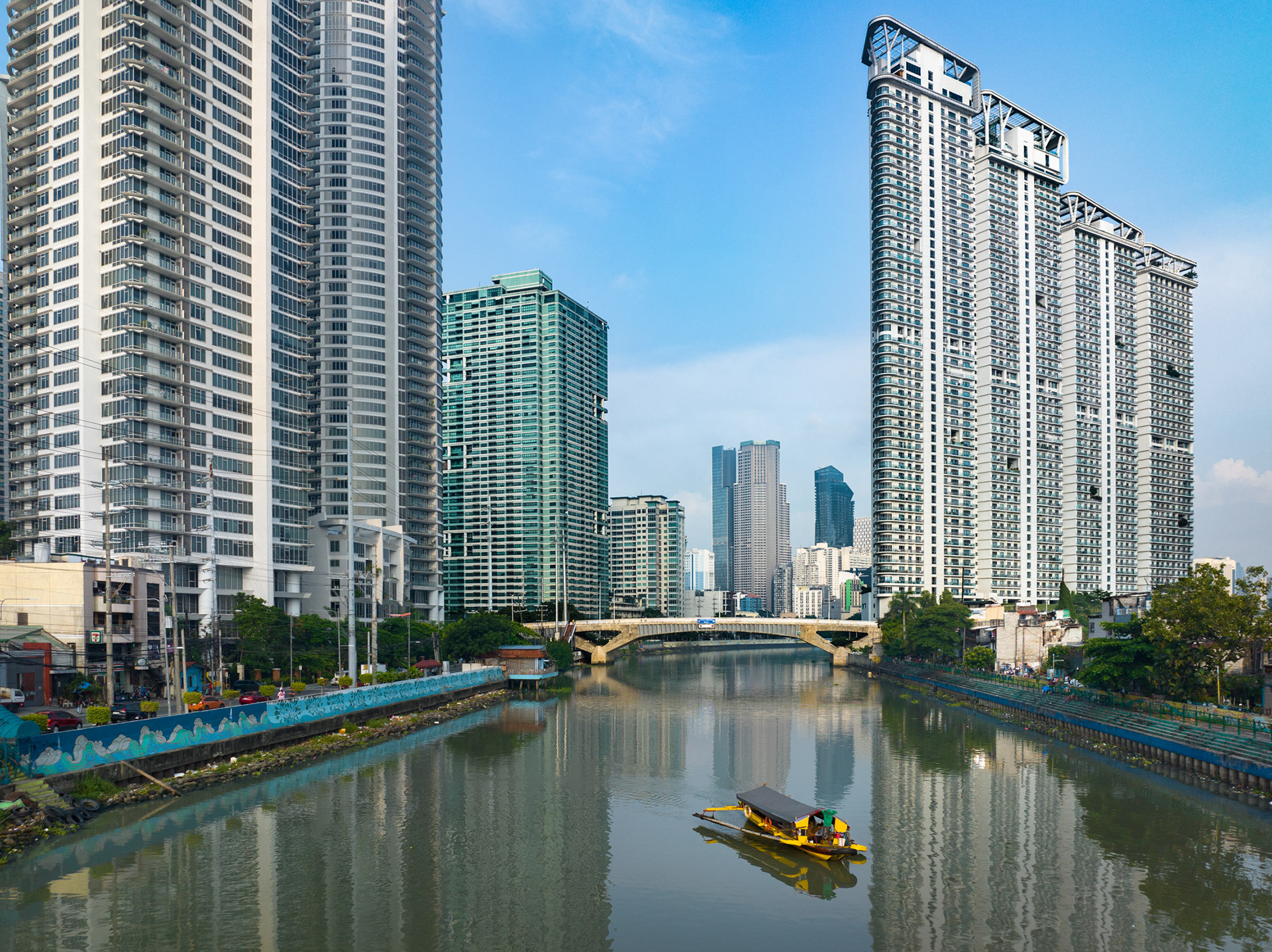 Photo of an informal ferry crossing the Pasig River in Manila, with modern high-rise towers of Makati in the background – highlighting disparities in transportation access.