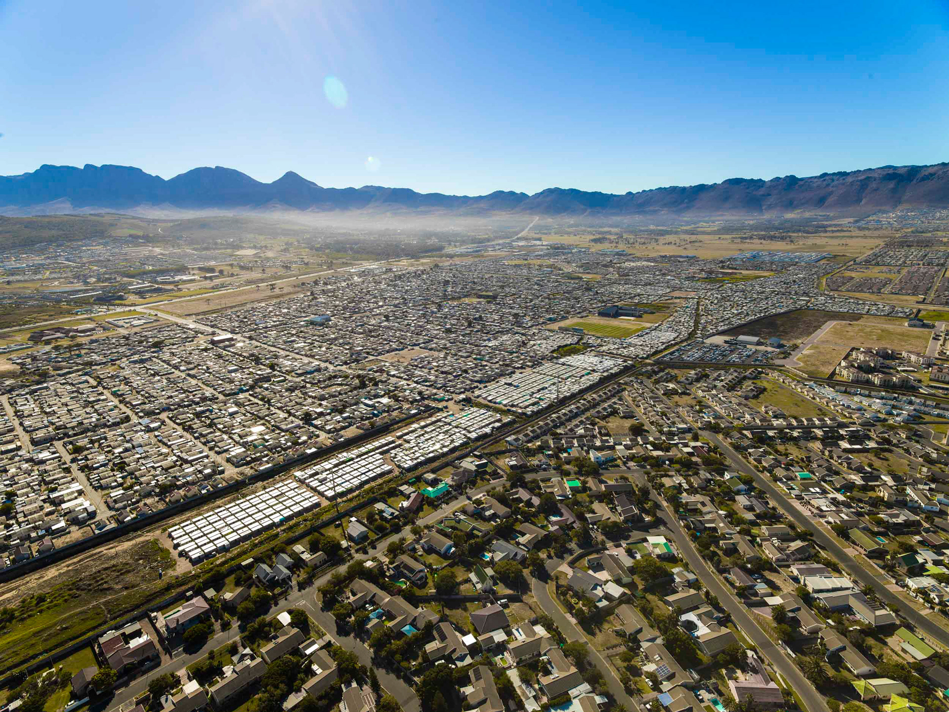 aerial view of shacks next to homes with mountains and winelands in cape town south africa