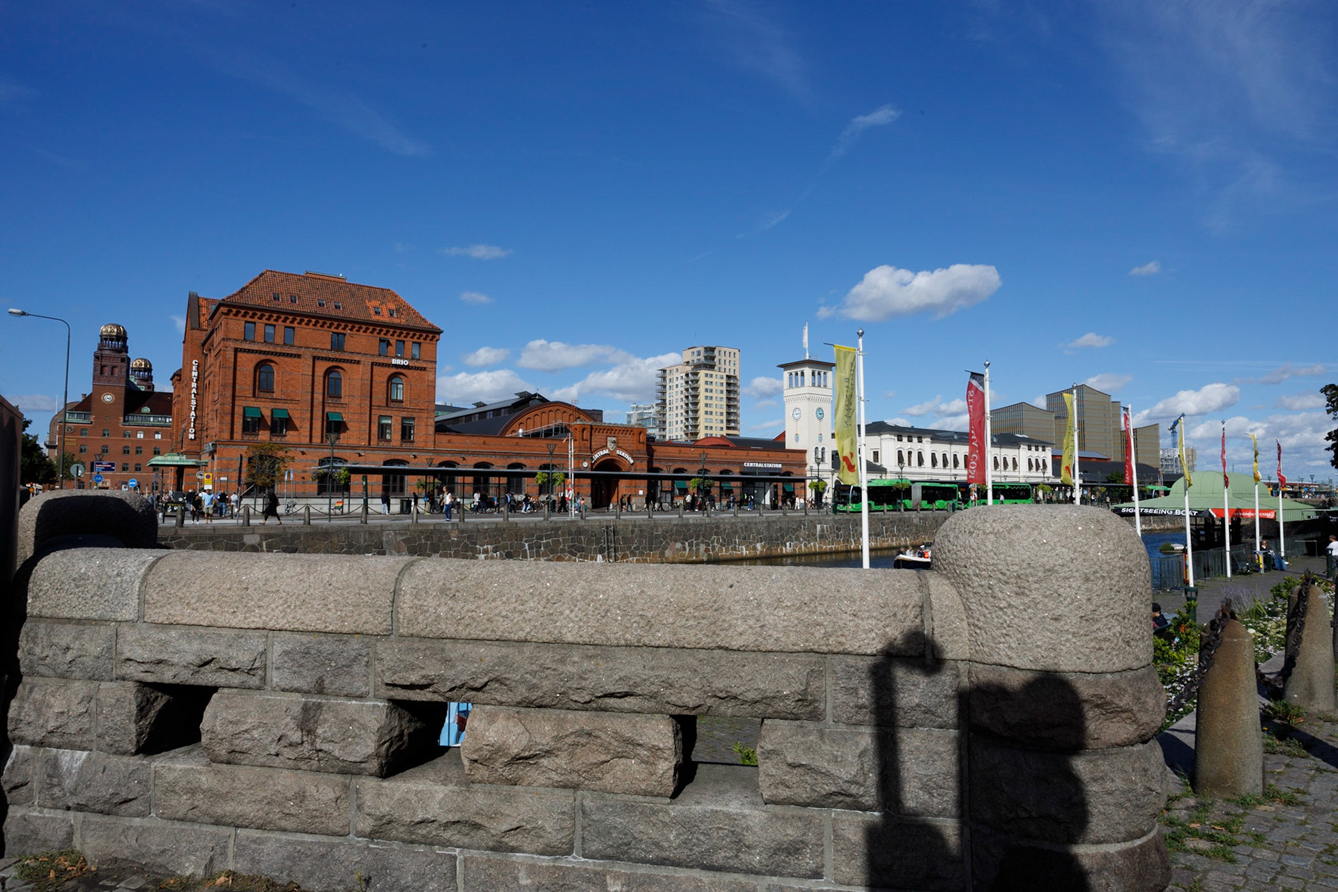 Malmö C med Mälarbron i förgrunden. Stationen invigdes 1858, men redan 1866 brann den ner och det vita tornet i bilden är det enda som är kvar från ursprungsbyggnaden. 1872 återinvigdes den nya stationen, den vita delen till vänster om tornet. Den röda byggnaden kommer från utbyggnaderna 1891 och 1924. Den senaste ombyggnaden skedd när Citytunneln togs i bruk 2010. Mälarbron som förbinder Hamngatan och Skeppsbron dagens stenbro byggdes 1914 och ersatte en tidigare järnbro.