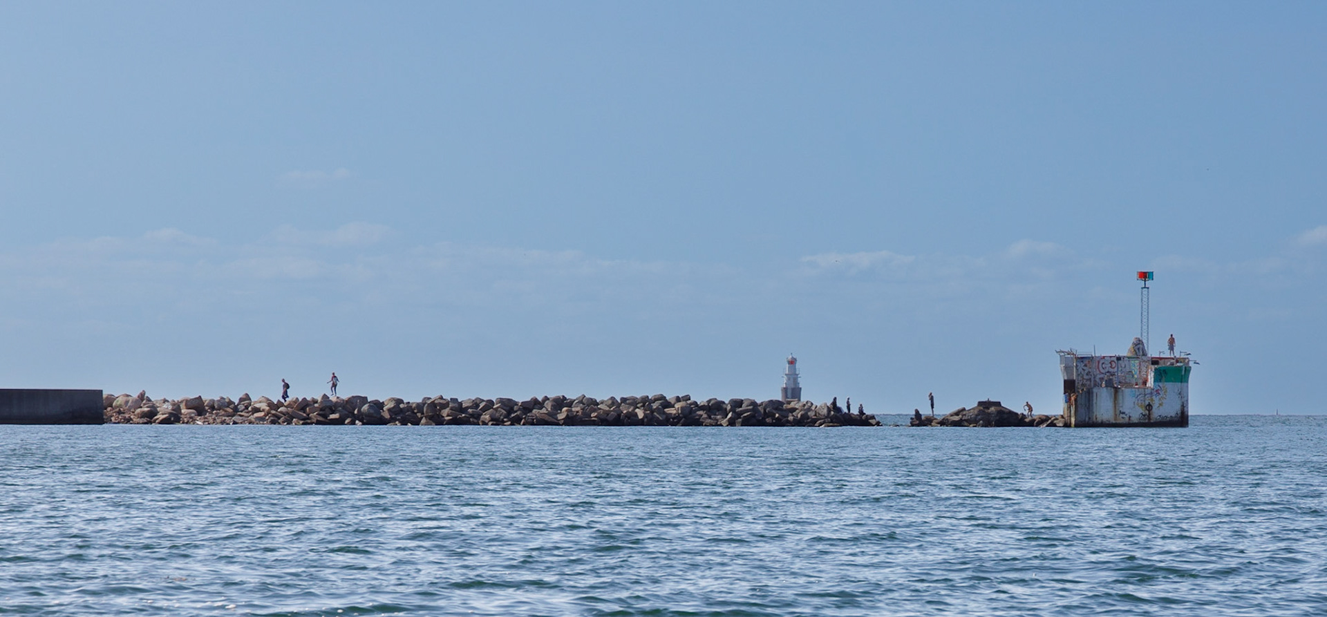 Varför bada på Ribban när man har en vågbrytare att bada från? Platsen är vid infarten till nuvarande Dockansplatsen. Fyren till höger heter MA 7 och byggdes 1937. Det en ledfyr som hjälper fartyg att lämna Frihamnen. Fyren i bakgrunden är Malmö Vågbrytarbank som leder fritt genom Trindelrännan och för utfarten från Industrihamnen. Trindelrännan går under lågbron på Öresundsbron öster om den djupare Flintrännan.