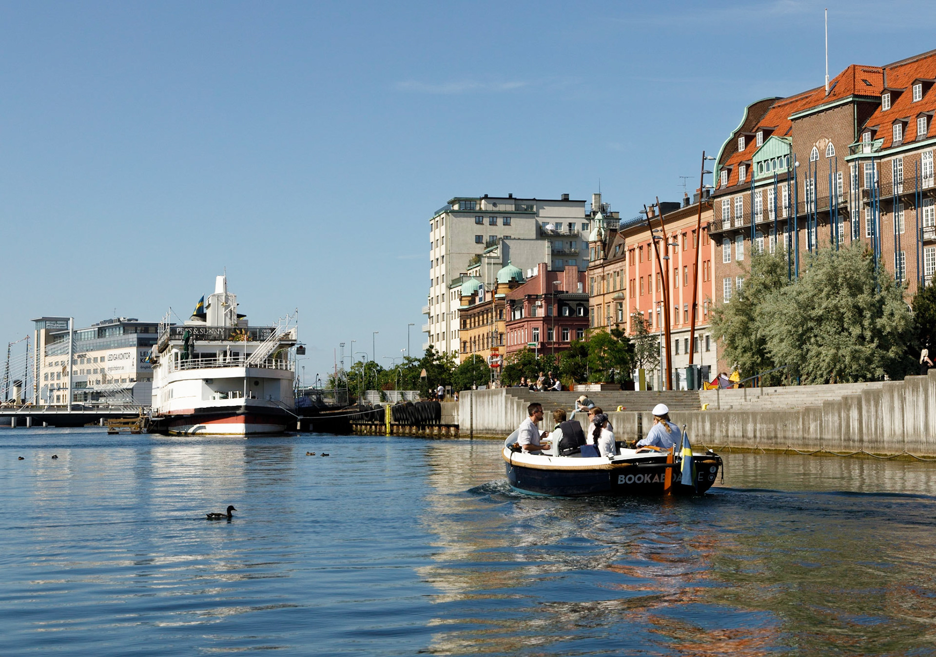 Inre hamnen. Förr var detta en livlig plats med båtar till Köpenhamn. Längst in låg de stora båtarna där man umder överfarten i lugn och ro kunde äta en god middag. Långre ut, dår den lilla båten passerar, låg Centrumlinjen. Flygbåtarna låg där den stora båten ligger. När de stora båtarna slutade att gå flyttade flygbåtarna in till deras hamnplats.  Idag går det inga stora båtar i Inre hamnen eftersom  en bro blockerar inloppet. I bakgrunden Smörkontrollen på Ångbåtsbryggan. Därifrån körde SAS svävare till Kastrup mellan 1984 och 1994 och därefter körde de katamaraner tills Öresundsbron öppnades.