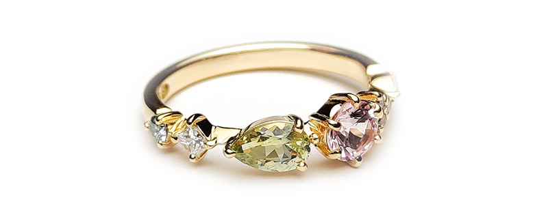 Tarina-sormus (kuva yllä). 18 k keltakulta. Kivet vasemmalta oikealle: 0.03 ct ice blue -timantti, 0.05 ct princess-hiontainen H vs -timantti, vaaleanvihreä pisarahiontainen Montana-safiiri, vaaleanpunainen Montana -safiiri, 3 x 0.01 ct champanjan väriset timantit, 0.05 ct markiisihiontainen H vs-timantti. Hinta 1850 euroa.
