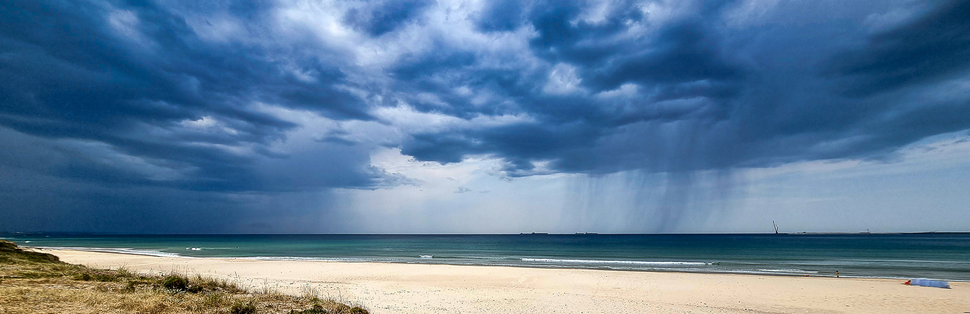 Dramatic storm clouds over the ocean with dark sky and rain approaching above a sandy beach.