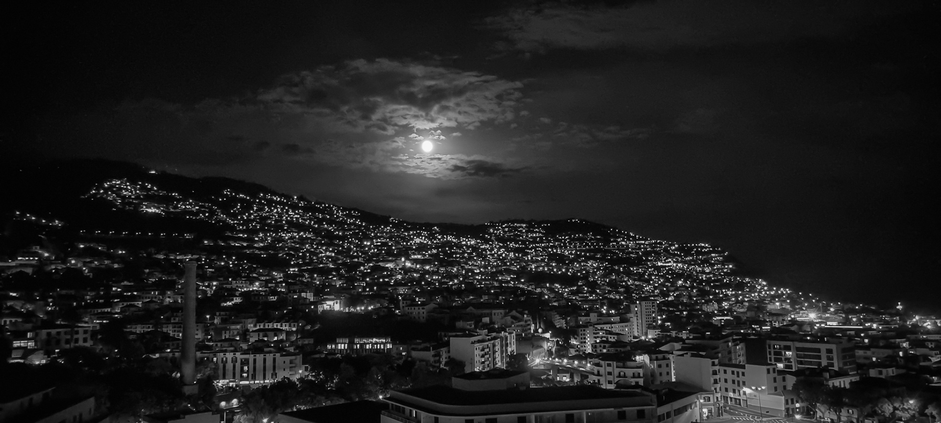 Black and white night photograph of Funchal illuminated beneath a moonlit sky, Madeira, Portugal.