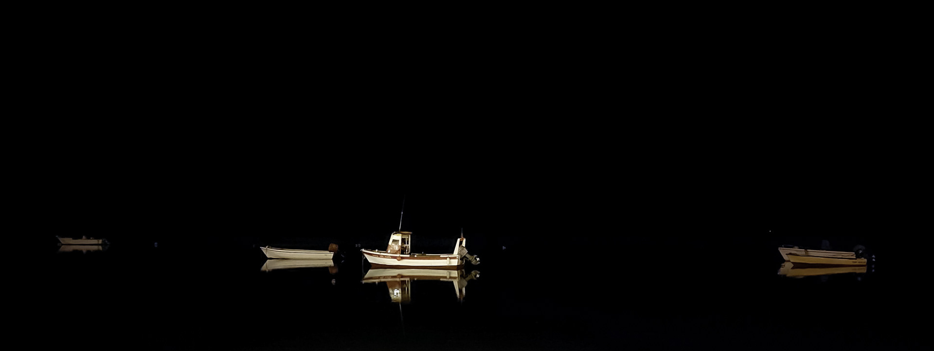 Minimalist night photograph of softly illuminated boats resting on dark still water.