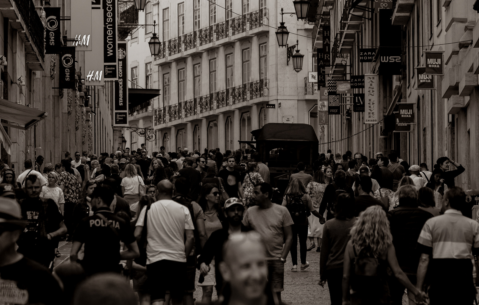 Busy pedestrian street in Lisbon with a dense crowd walking in both directions, captured in black and white.