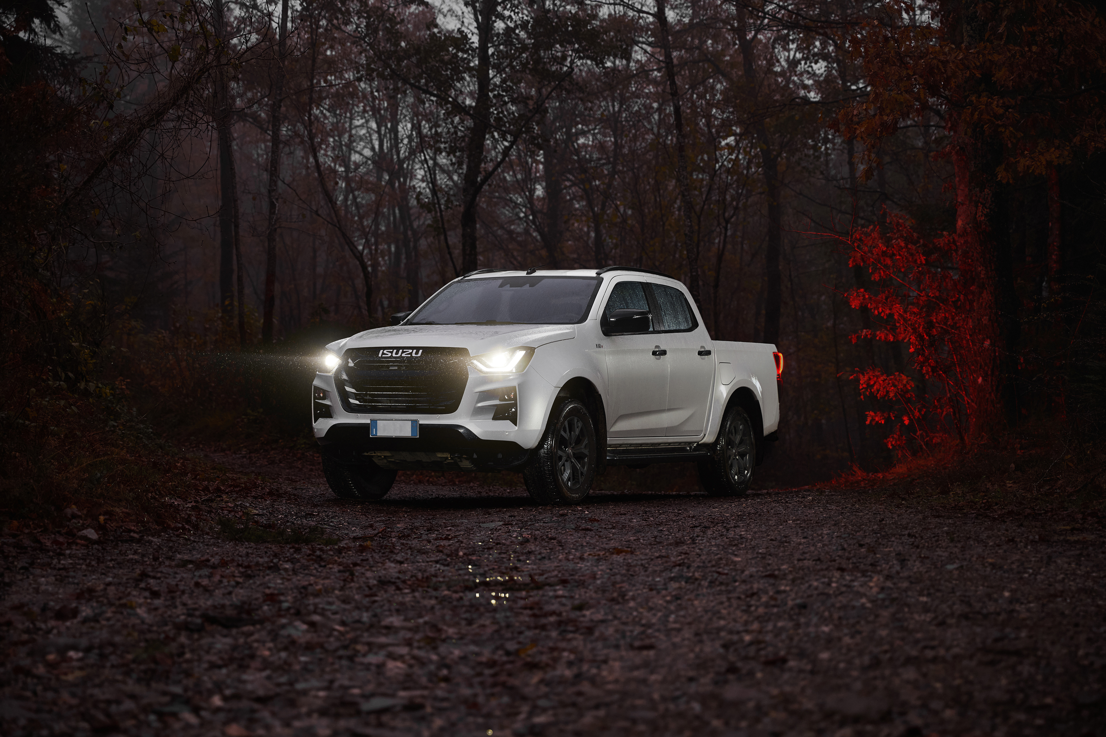 Isuzu D’max FF 2024. I riflessi delle gocce e l’illuminazione sapientemente dosata evidenziano le linee robuste e muscolose del veicolo, rendendolo protagonista assoluto di un paesaggio avvolto da tonalità scure e misteriose. Un’immagine che celebra l’avventura, la potenza e la connessione con gli elementi.
