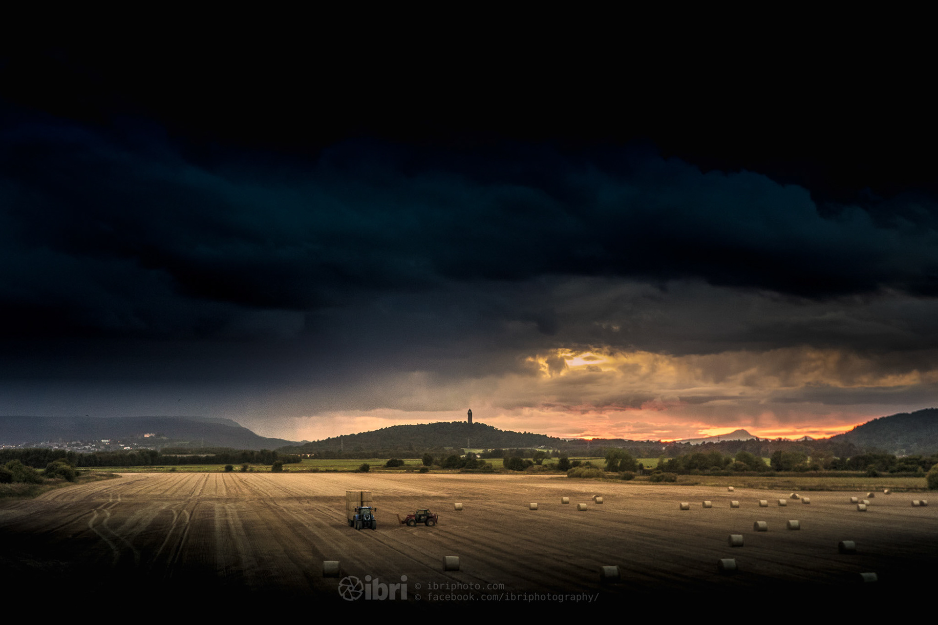 A fiery sunset behind Wallace Monument, Stirling, as the harvesting continues into the twilight.