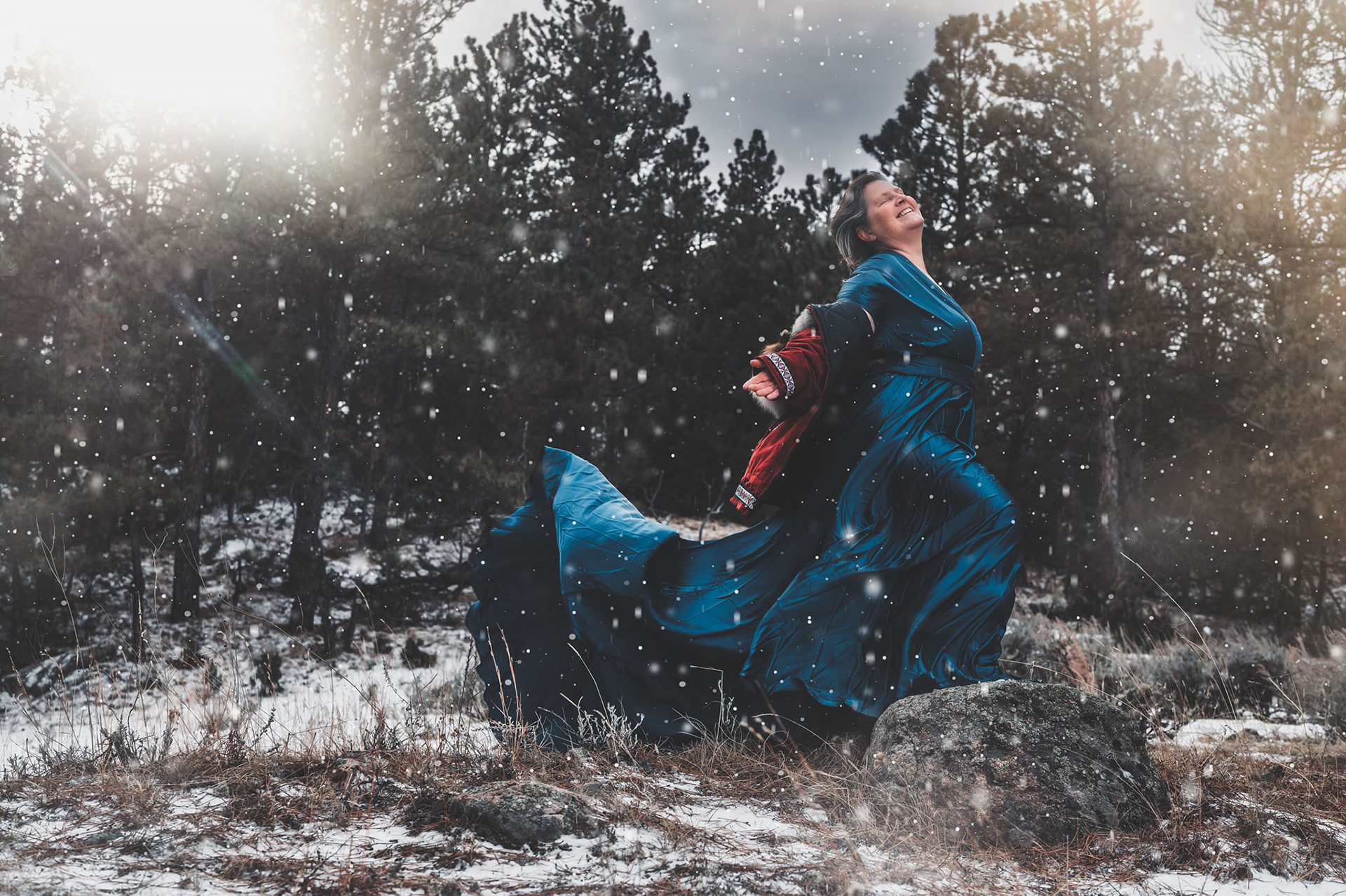 Color CCPLLC Cheyenne WY Intimate Portrait of woman in the snow wearing dramatic blue dress and red parka smiling, wind blown, older woman