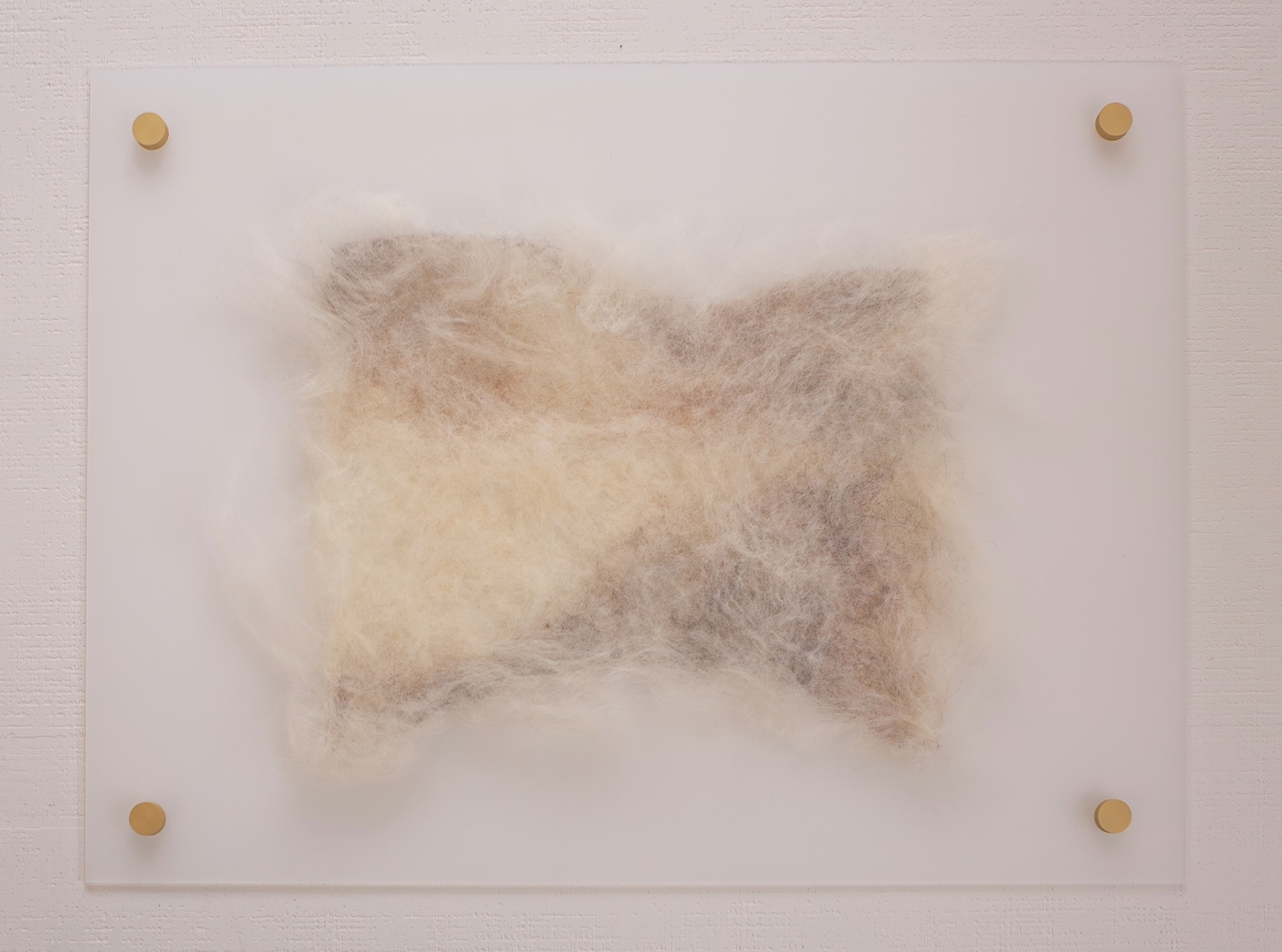 “The Space In-Between” wool relief in cream, tan, and gray floating on a milky acrylic panel mounted with four gold standoffs on a white textured wall.