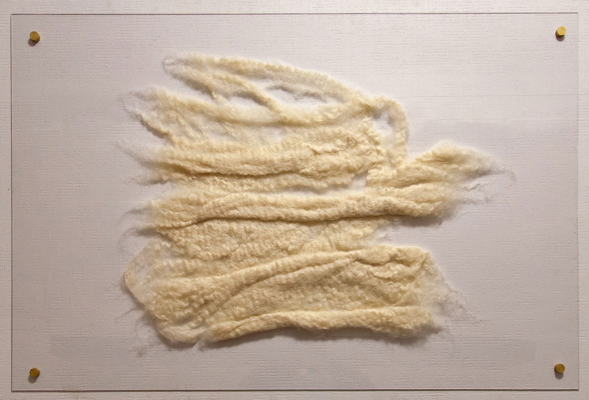 Cream-colored felted wool bands arranged in a birdlike form, mounted on a clear polycarbonate panel with four matte gold standoffs against a white wall.