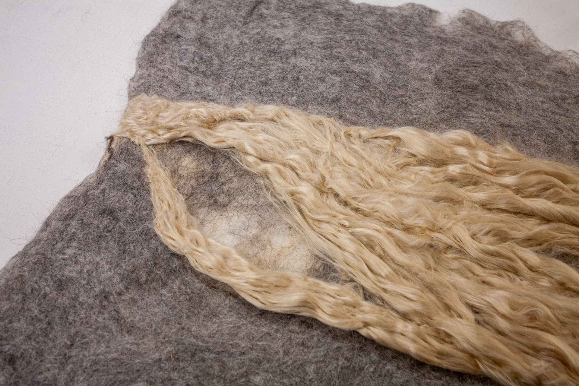 Angled detail of the silk oval opening within the gray wool felt, highlighting layered fibers and the subtle negative-space window.