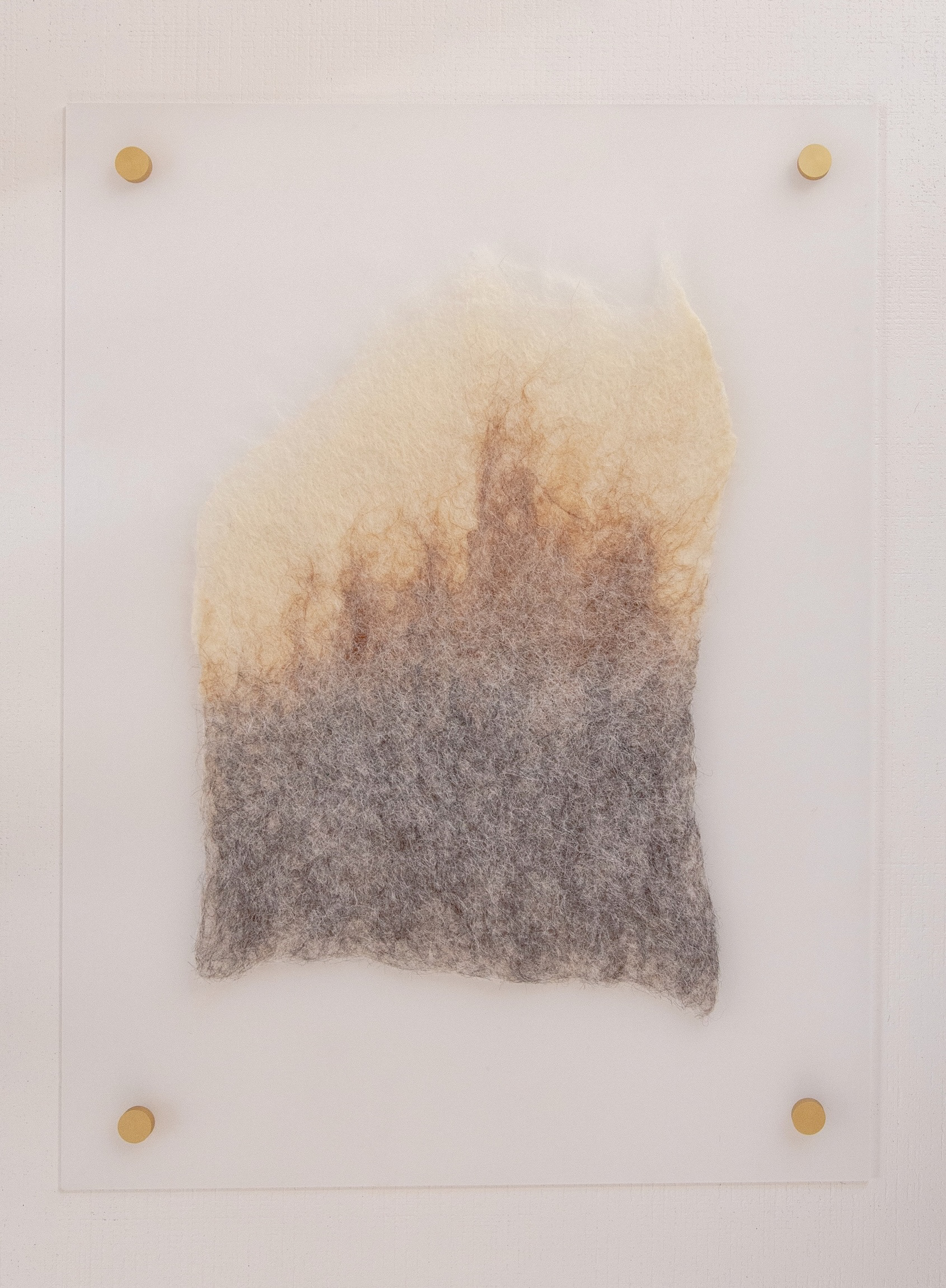 Hand-felted fiber wall relief in gray, rust, and cream tones floating on a clear acrylic panel, mounted with four matte gold standoffs against a white wall.