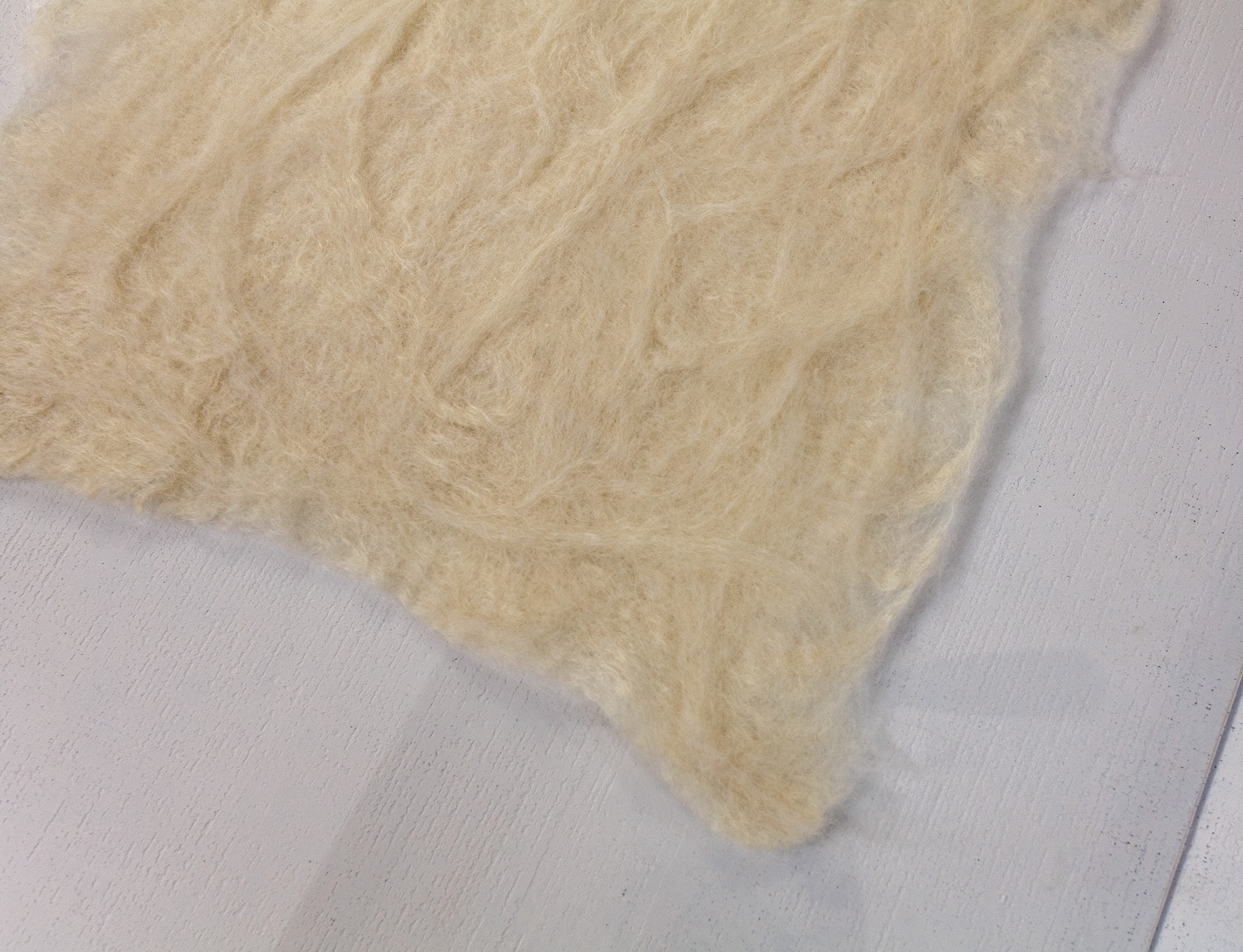 Close-up of the wool relief’s lower edge on clear polycarbonate, showing soft layered fibers and subtle shadow along the panel.