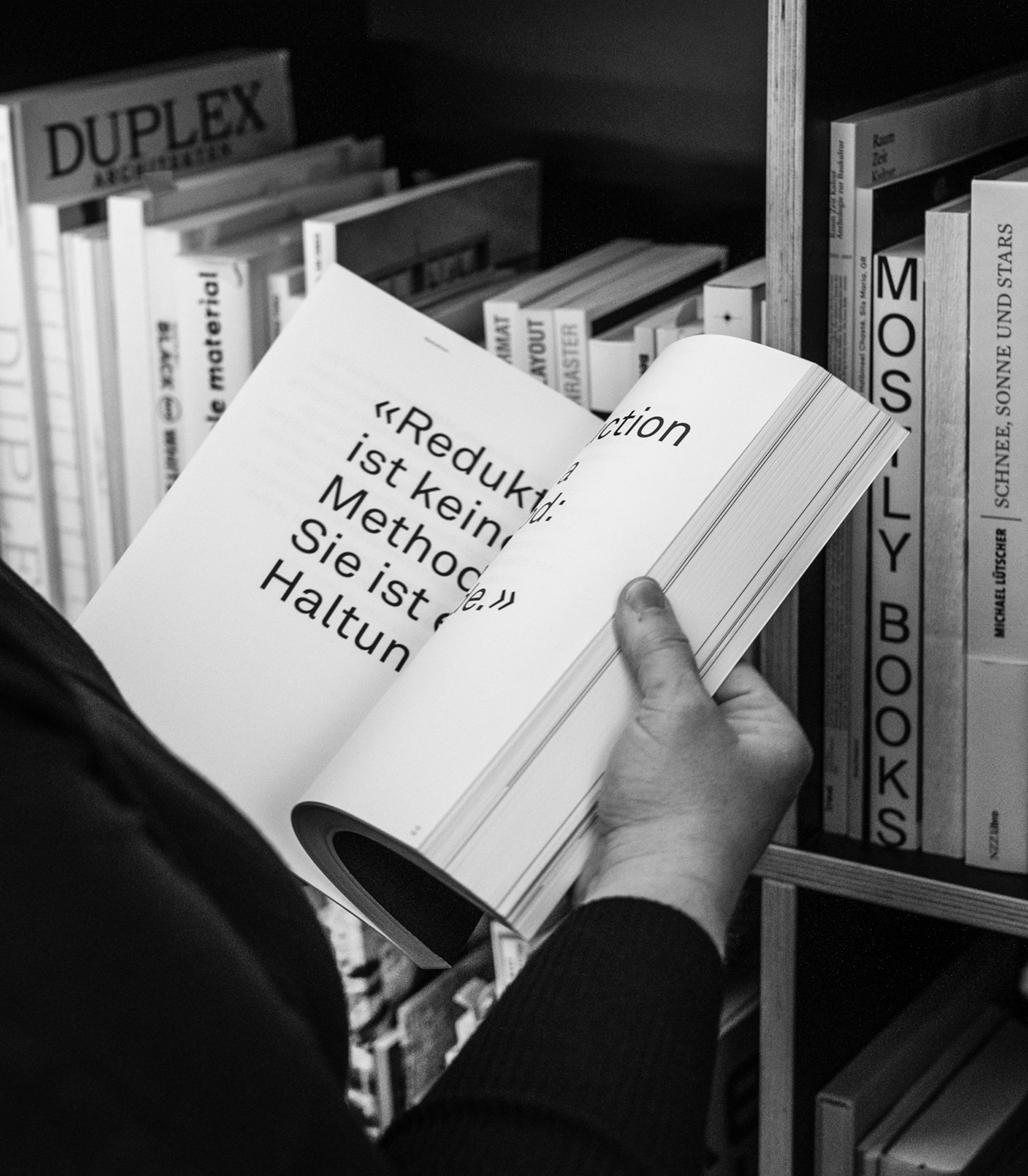 Nicole Giesch steht vor dem Büchergestell und hält ein aufgeschlagenes Buch von Armin Hofmann in der Hand: Reduktion ist keine Methode. Sie ist eine Haltung.