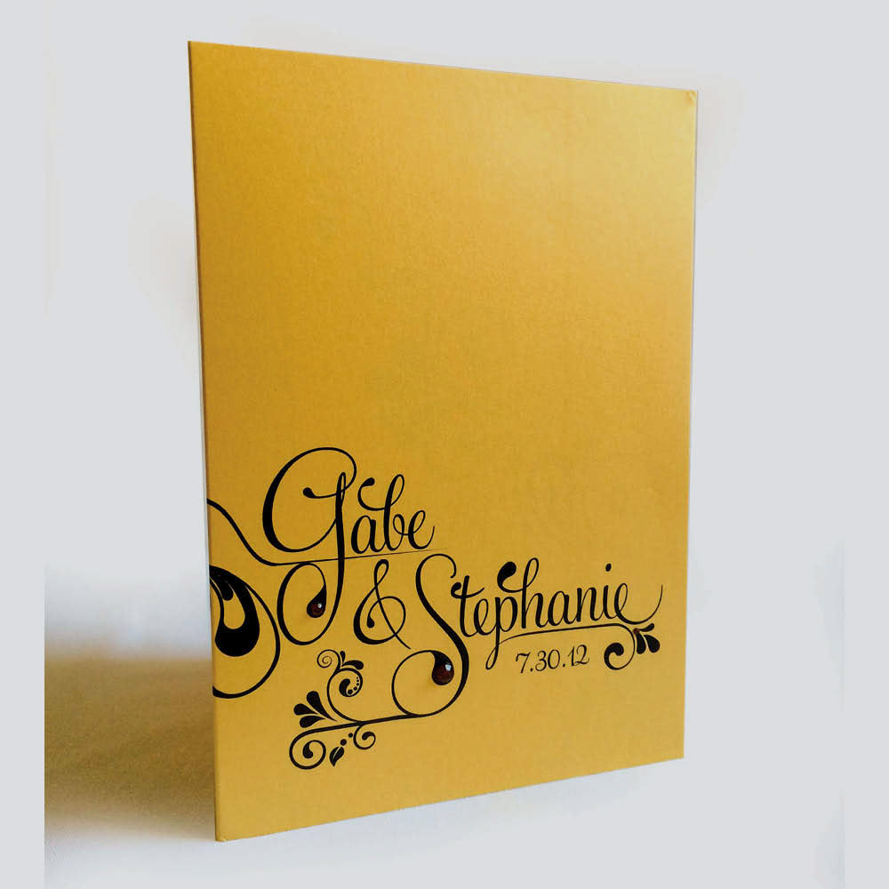 This bride had an extremely limited budget, but she wanted to incorporate an organic design element like vines or leaves using gold, black, white, and red. I chose gold metallic stock and added small, dark red rhinestones to the cover.