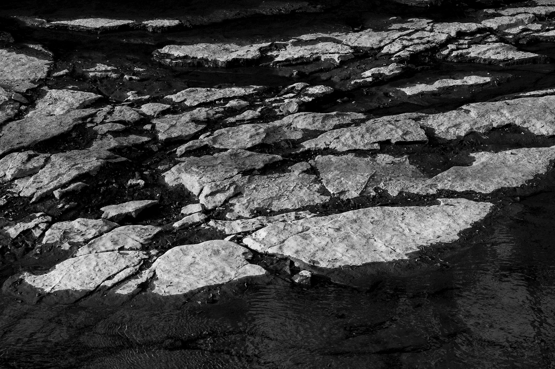 Rock formations meeting soft ripples of water in monochrome tones. Fine art photograph by Ryan Bucchianeri.