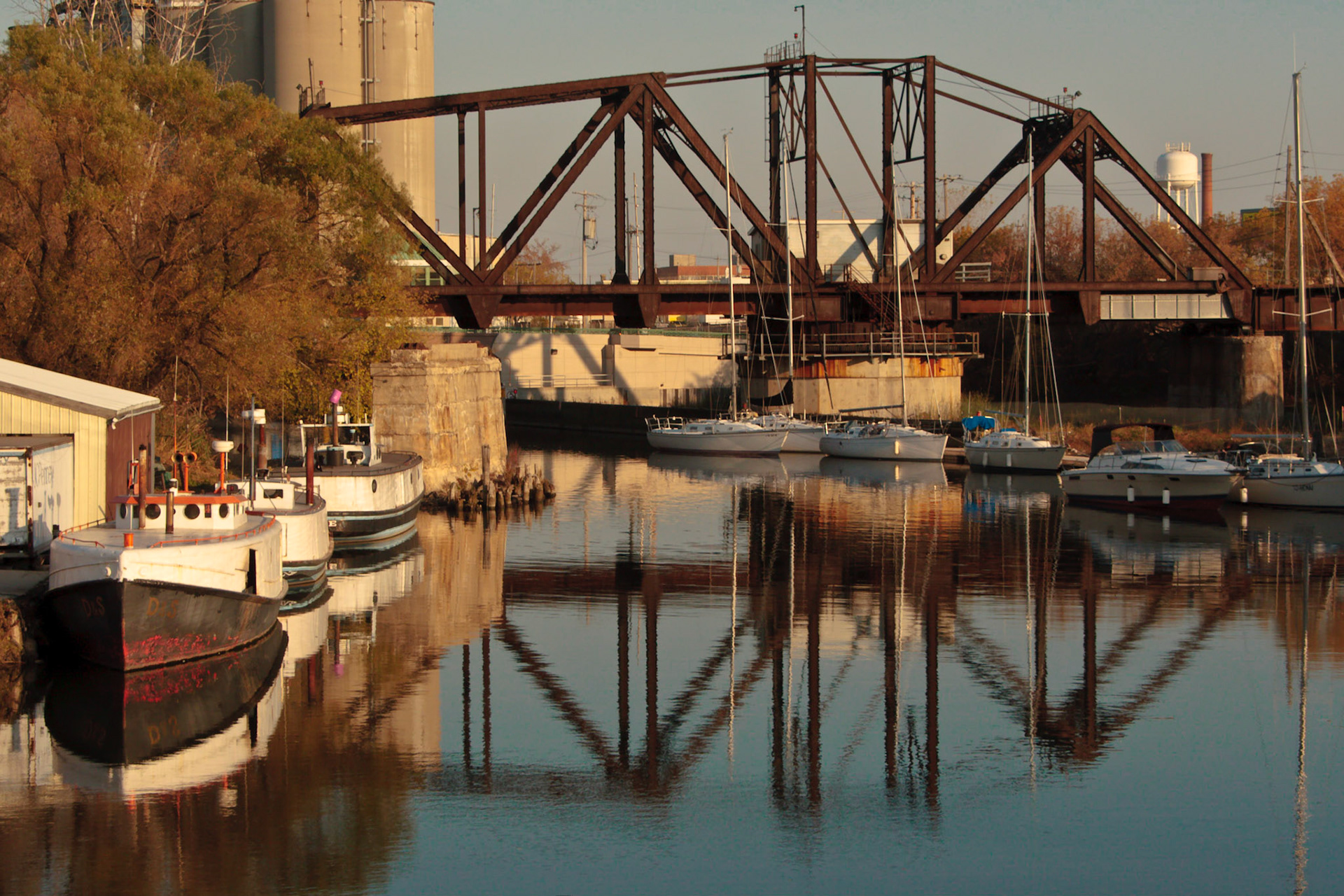 A late afternoon shot of the Kinnickinnick River in Milwaukee, Wisconsin, showing numerous small craft in the shadow of a railway bridge.