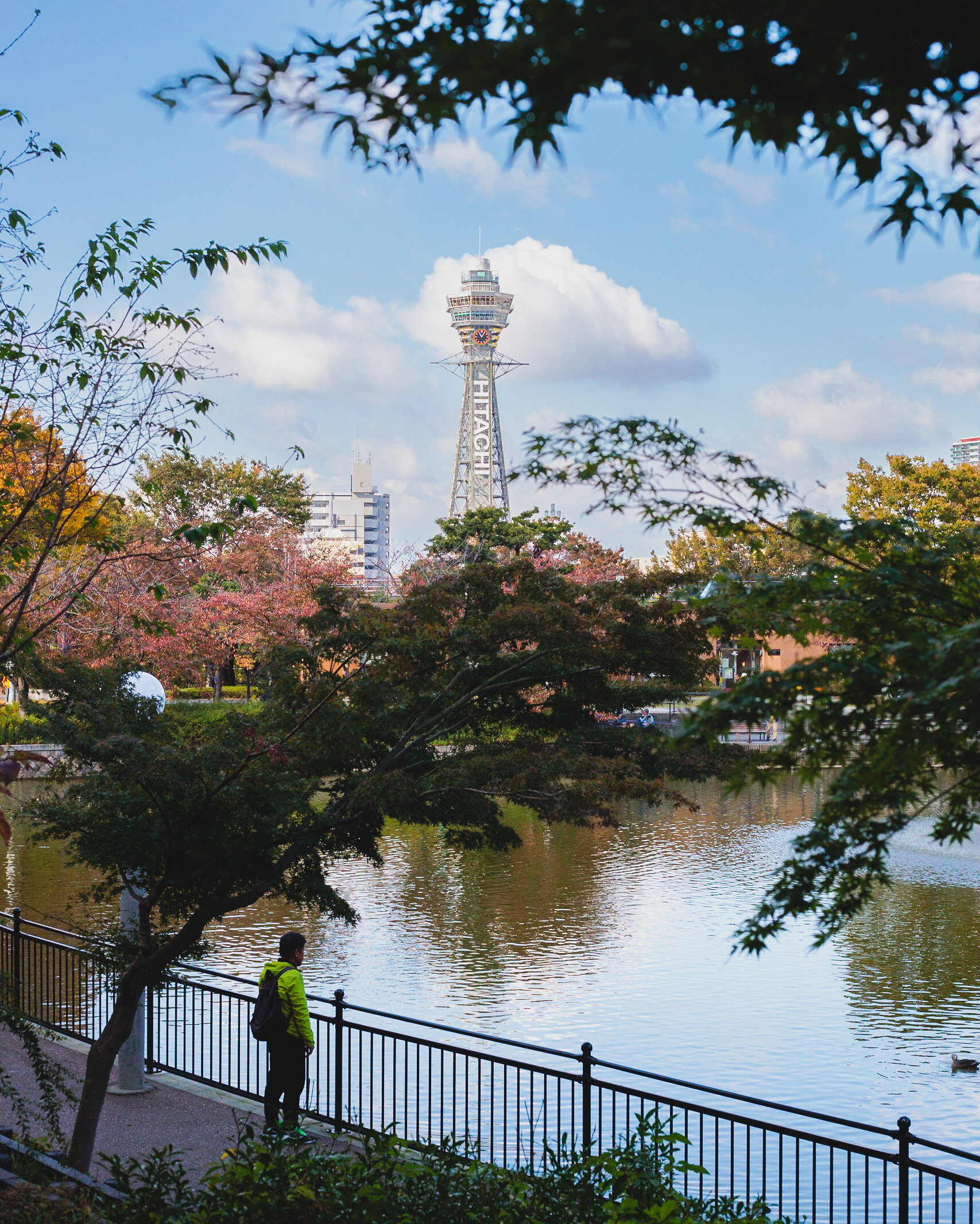 A man watching the pond in Tennoji Park with the Tsutenkaku in the background.