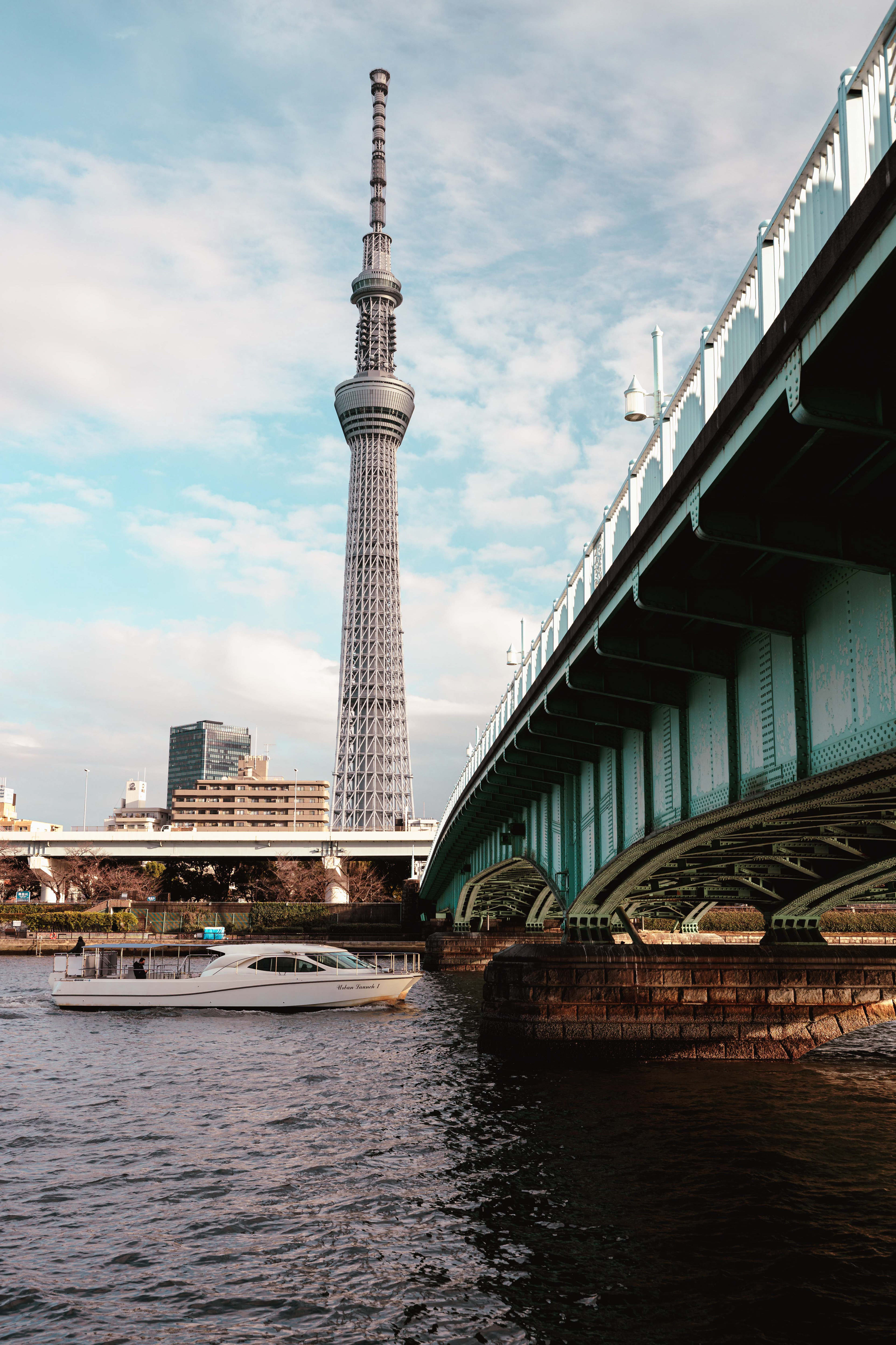 The Skytree in Tokyo with a boat passing under a bridge.