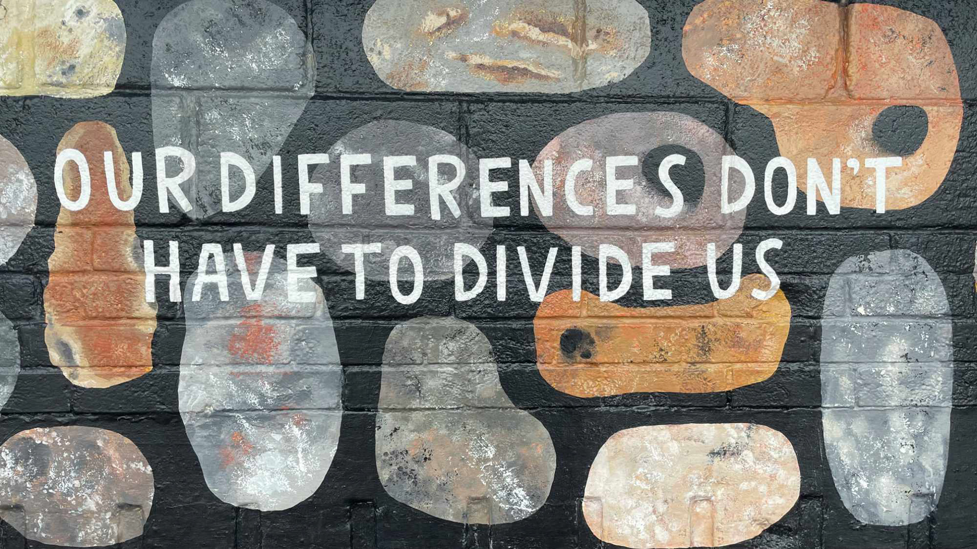 The words "Our differences don't have to divide us" handwritten in white on a wall painted back with shapes.