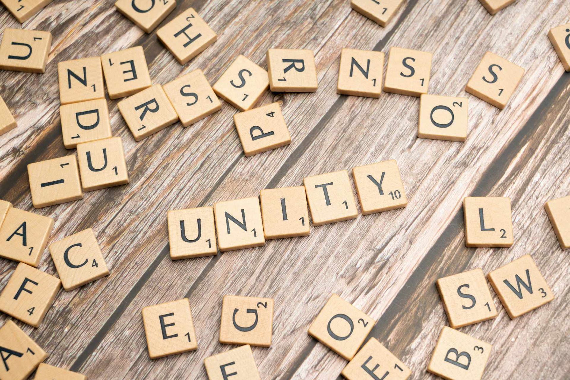 Scrabble blocks spelling the word "UNITY" among random letters on a wooden table.