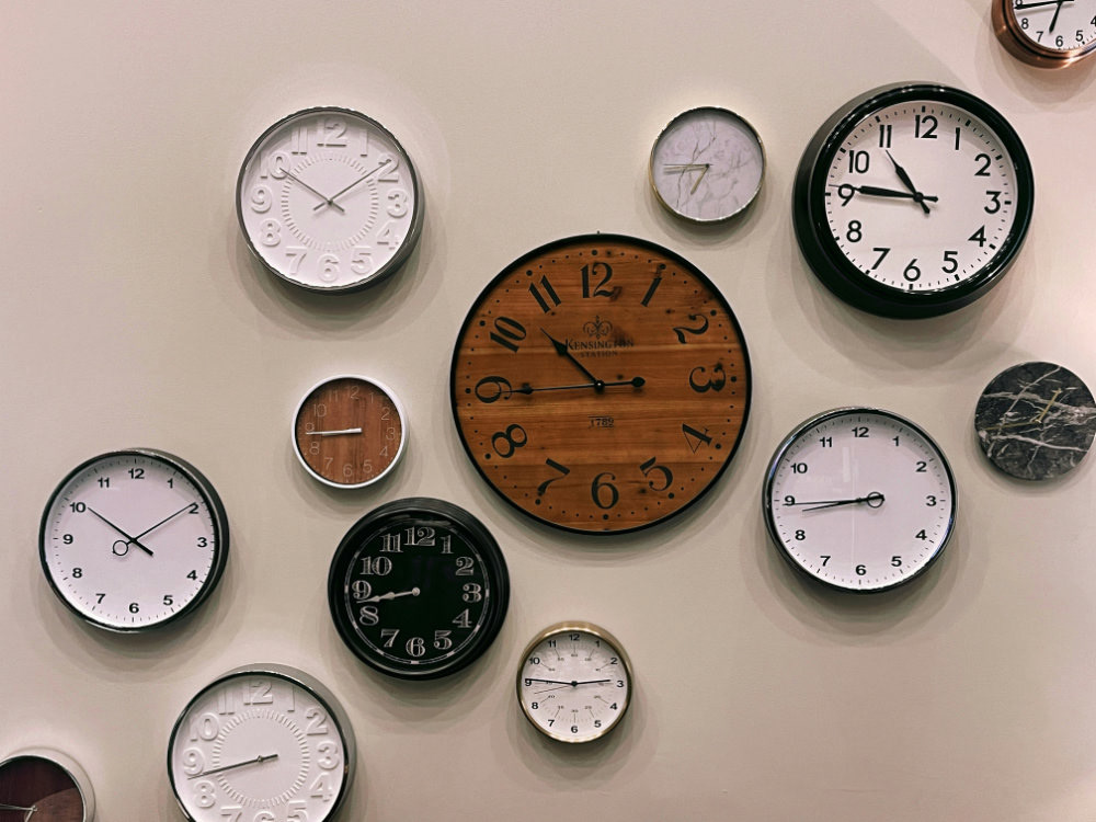 Many different sized and coloured wall clocks on a beige wall.