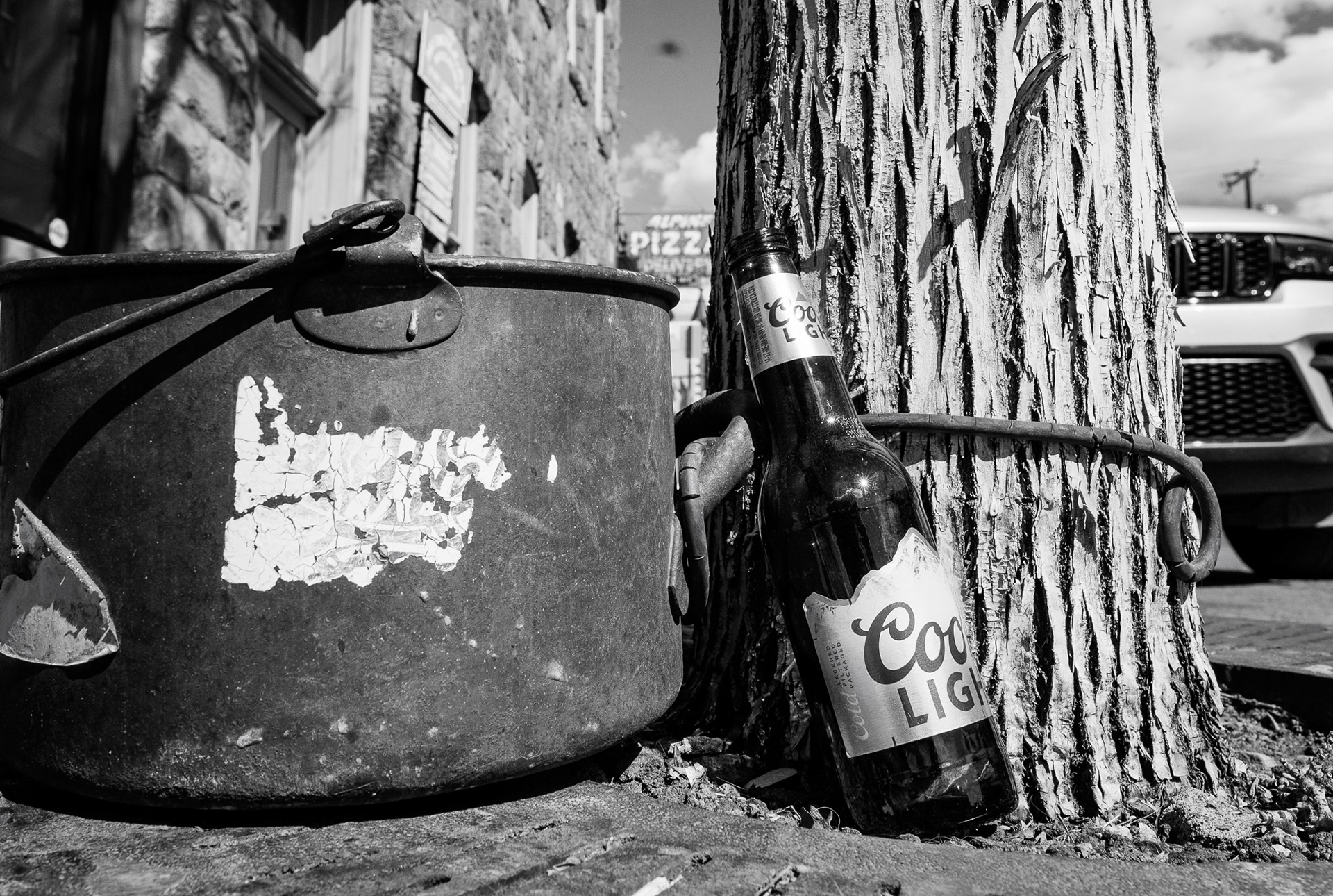 A bottle of Coors Light lays by a bucket outside of Alpine Pizza in downtown Flagstaff. I was a real fan of how this was just sitting here casually like this. It was sitting in such a perfect spot when it comes down to the exposure and composition of the image. The light was hitting the tree at such a perfect angle where it made the tree and bucket have the most fantastic texture. Plus there is an itty bitty sunburst in the side of the bottle that I really think adds something extra to the image. Taken on the Sigma 20mm f/1.4 art lens. March 5, 2026.