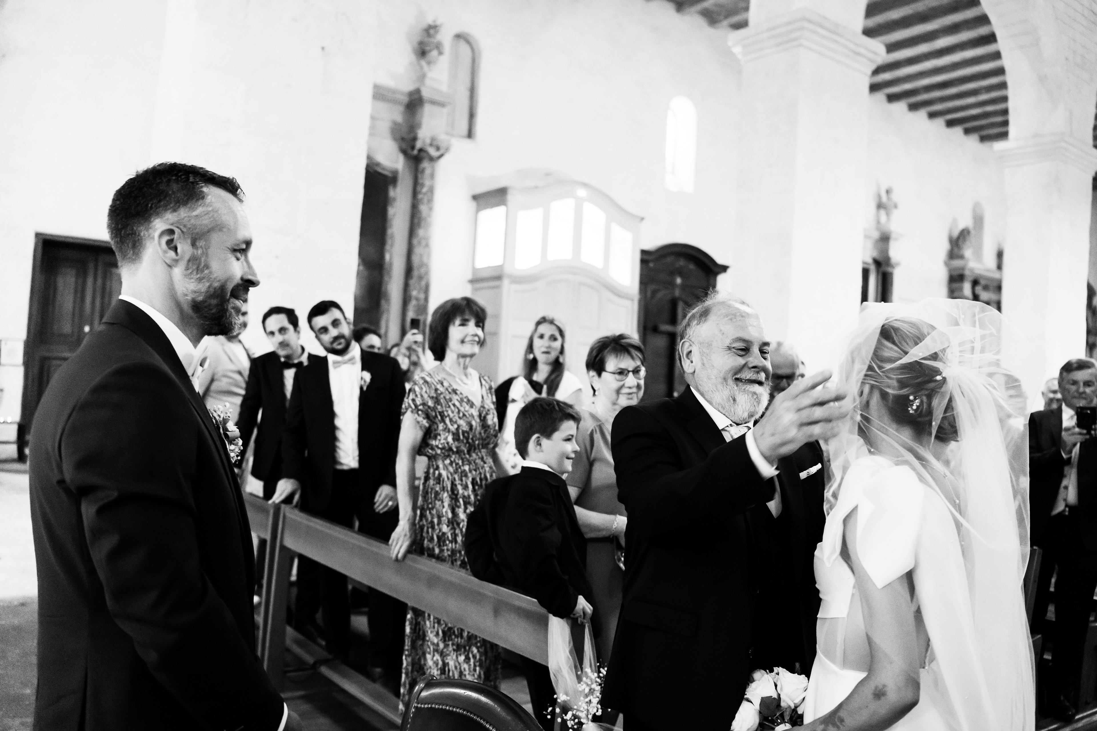 Le père soulève le voile de la mariée tandis que le marié la regarde avec émotion pendant la cérémonie à Béziers