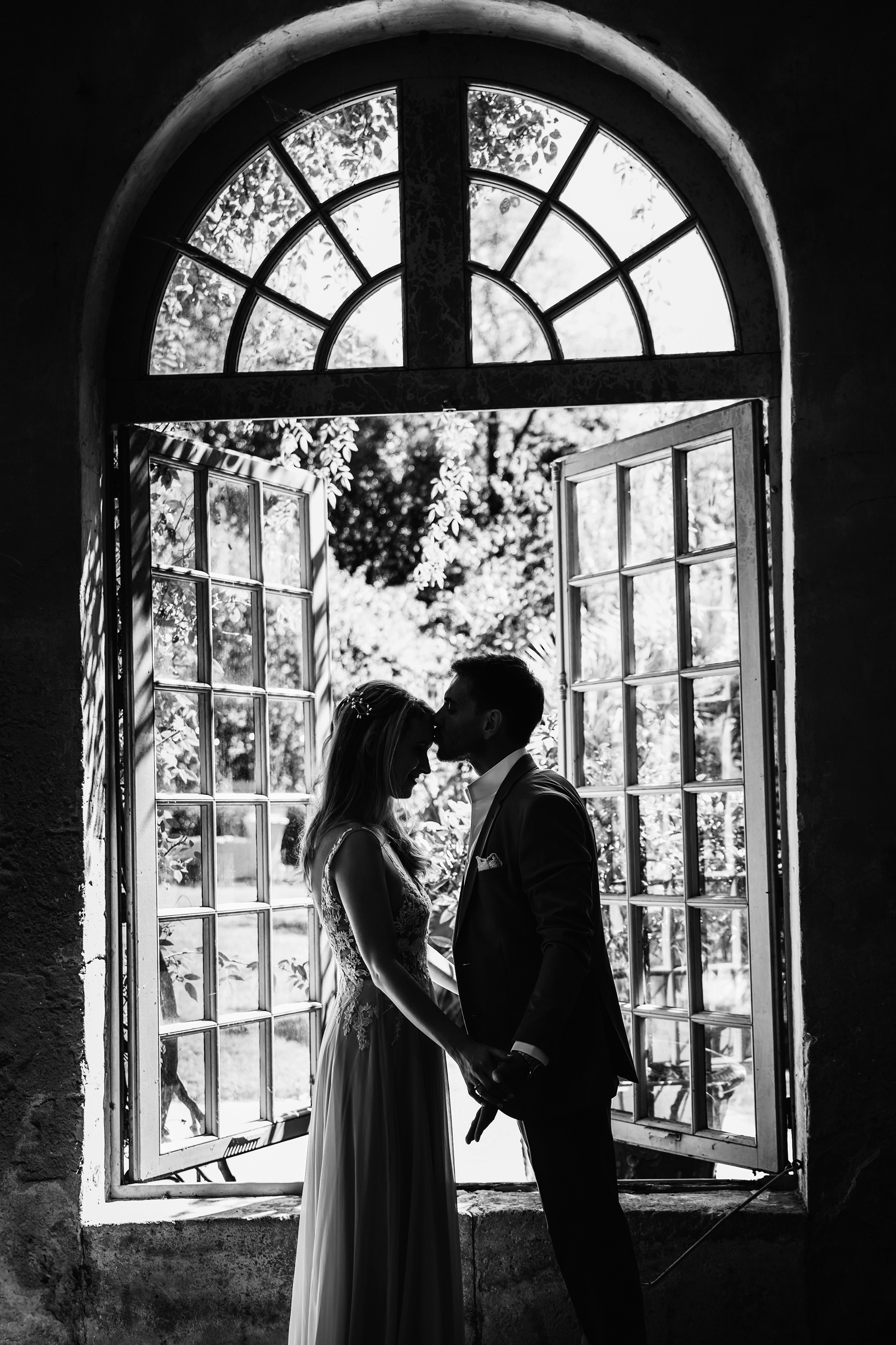 couple en noir et blanc s’embrassant devant une fenêtre à petits carreaux, photo en contre-jour au Château de Flaugergues Montpellier