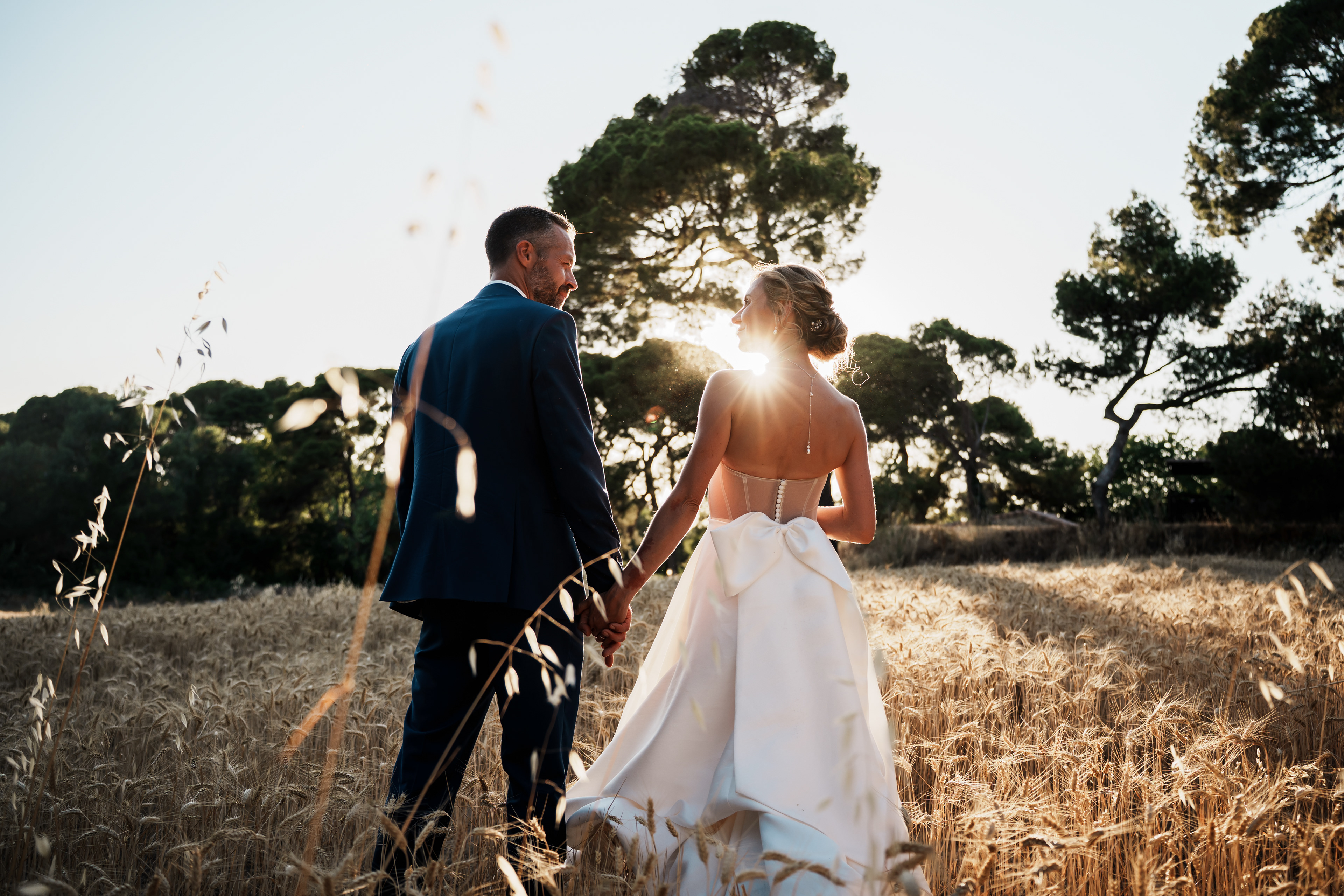 Couple de mariés de dos dans un champ de blé au coucher de soleil, moment intime et naturel