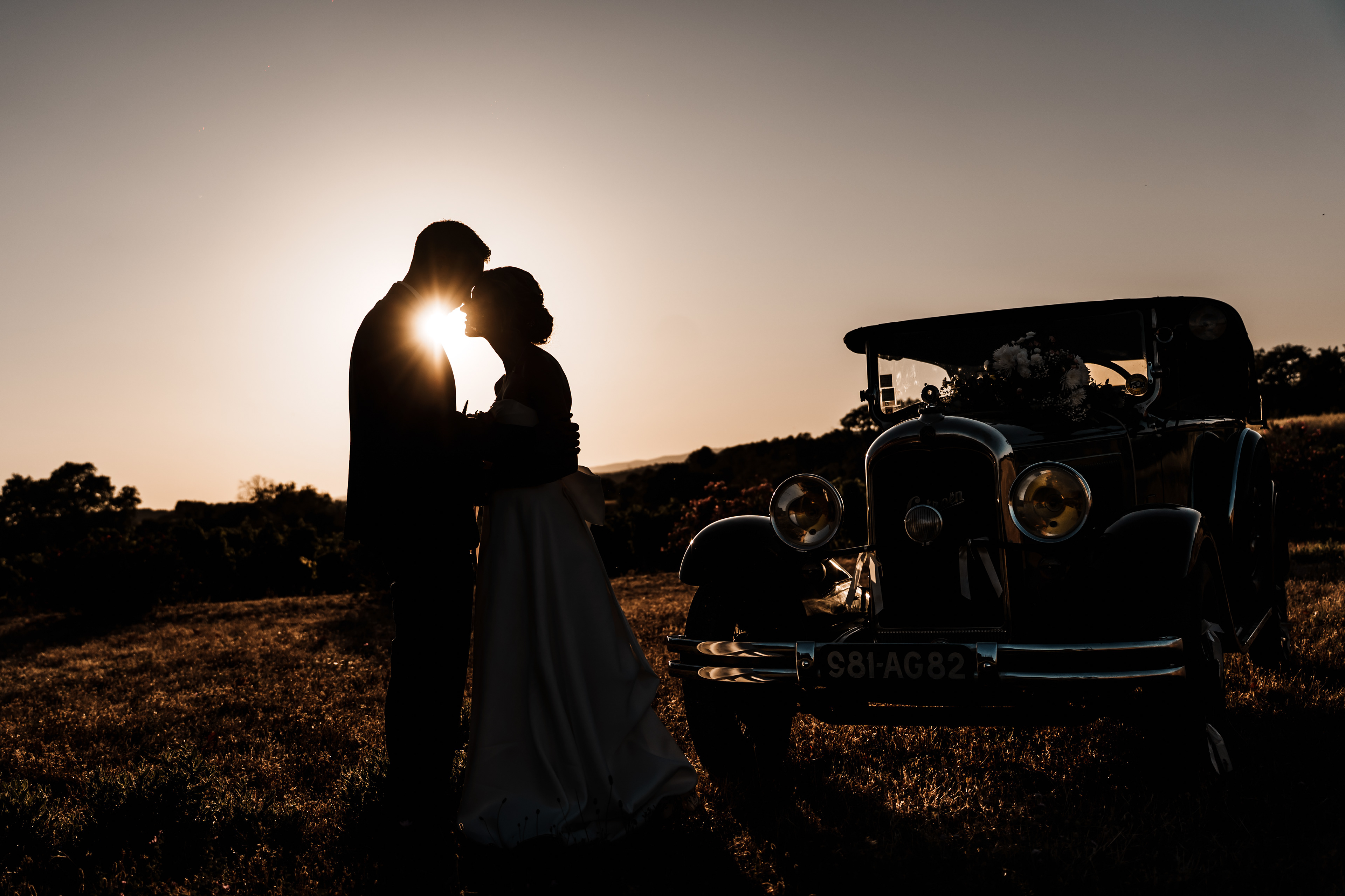 Les mariés à côté d’une voiture de collection au coucher de soleil lors d’une séance photo de mariage dans l’Hérault
