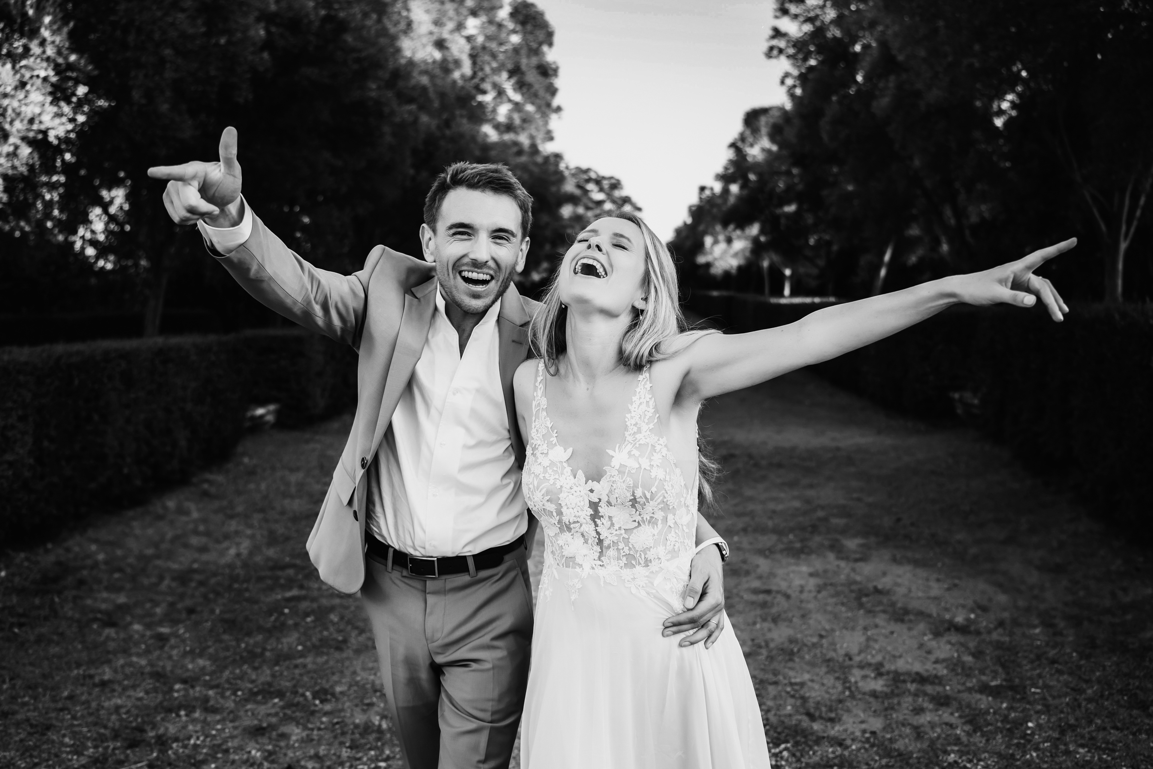 couple marié en noir et blanc marchant bras ouverts, moment de joie et de complicité au Château de Flaugergues à Montpellier