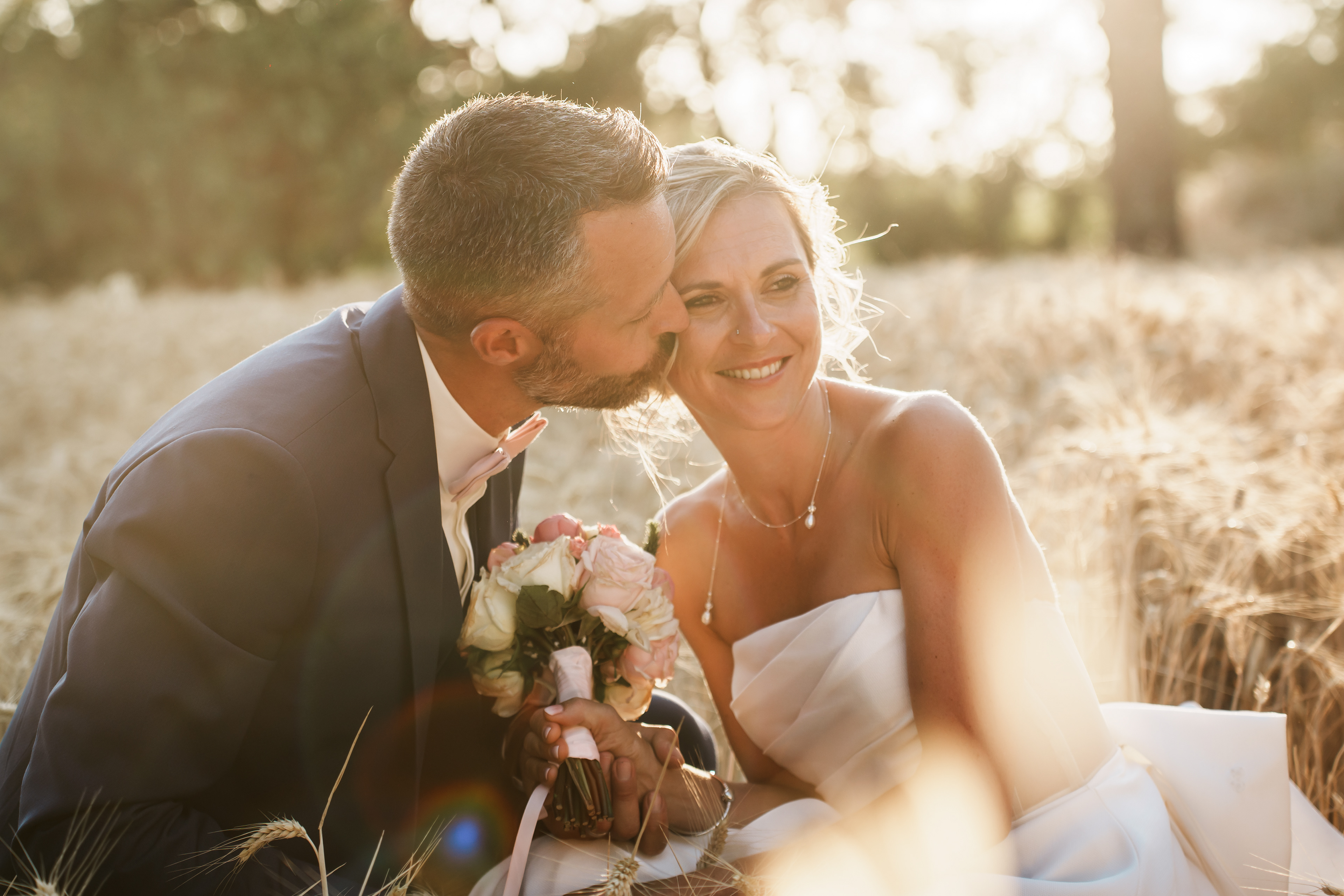 Moment tendre où le marié dépose un bisou sur la joue de la mariée pendant la séance photo au coucher de soleil