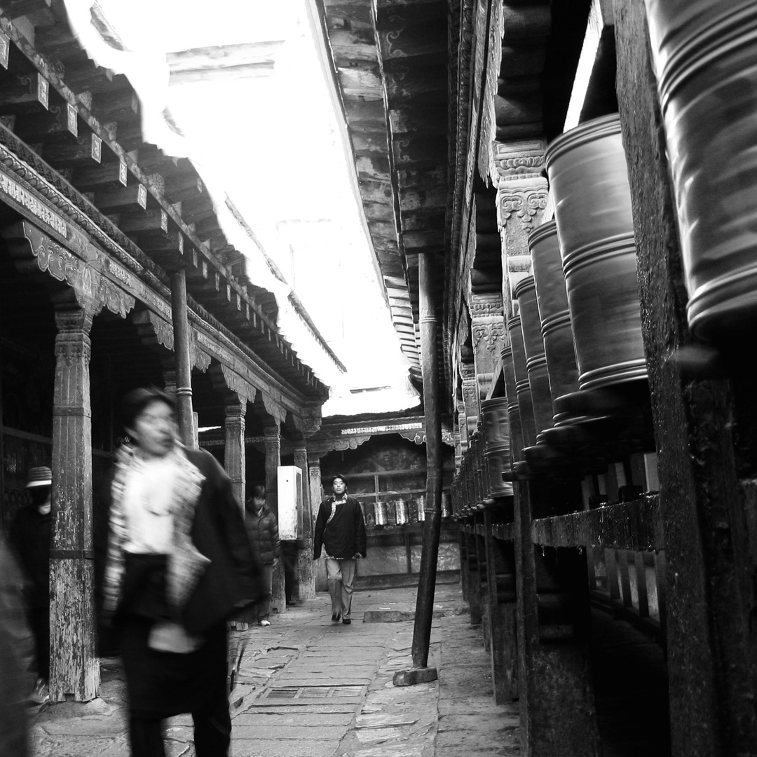 Pilgrims circulate through a monastery corridor lined with prayer wheels, an act of daily worship rooted in Tibetan Buddhist tradition. Lhasa, China