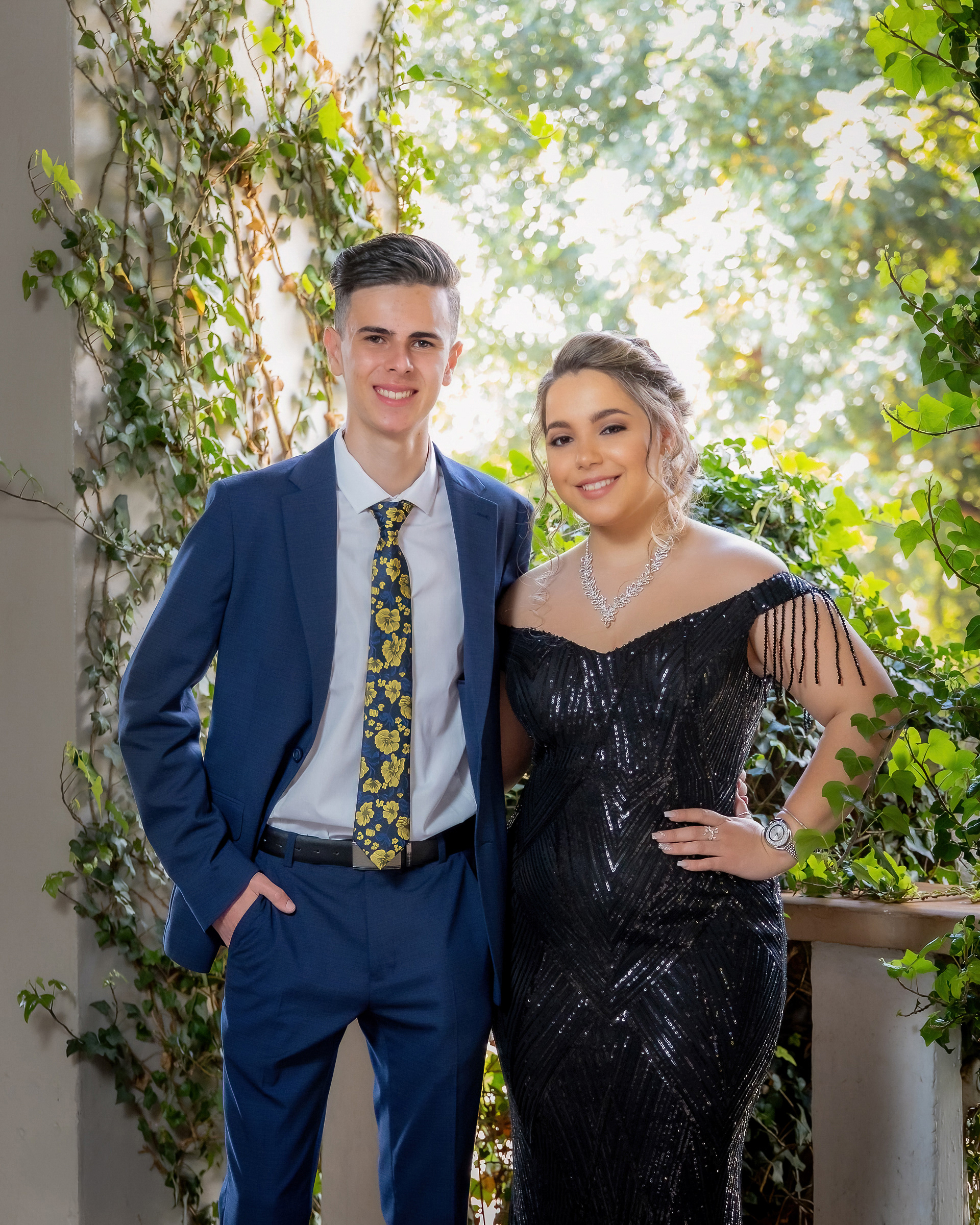 Ivan Muller Photography: A matric farewell couple standing together, the girl in a sparkling black off-the-shoulder dress and the boy in a sharp blue suit with a floral tie, Centurion.