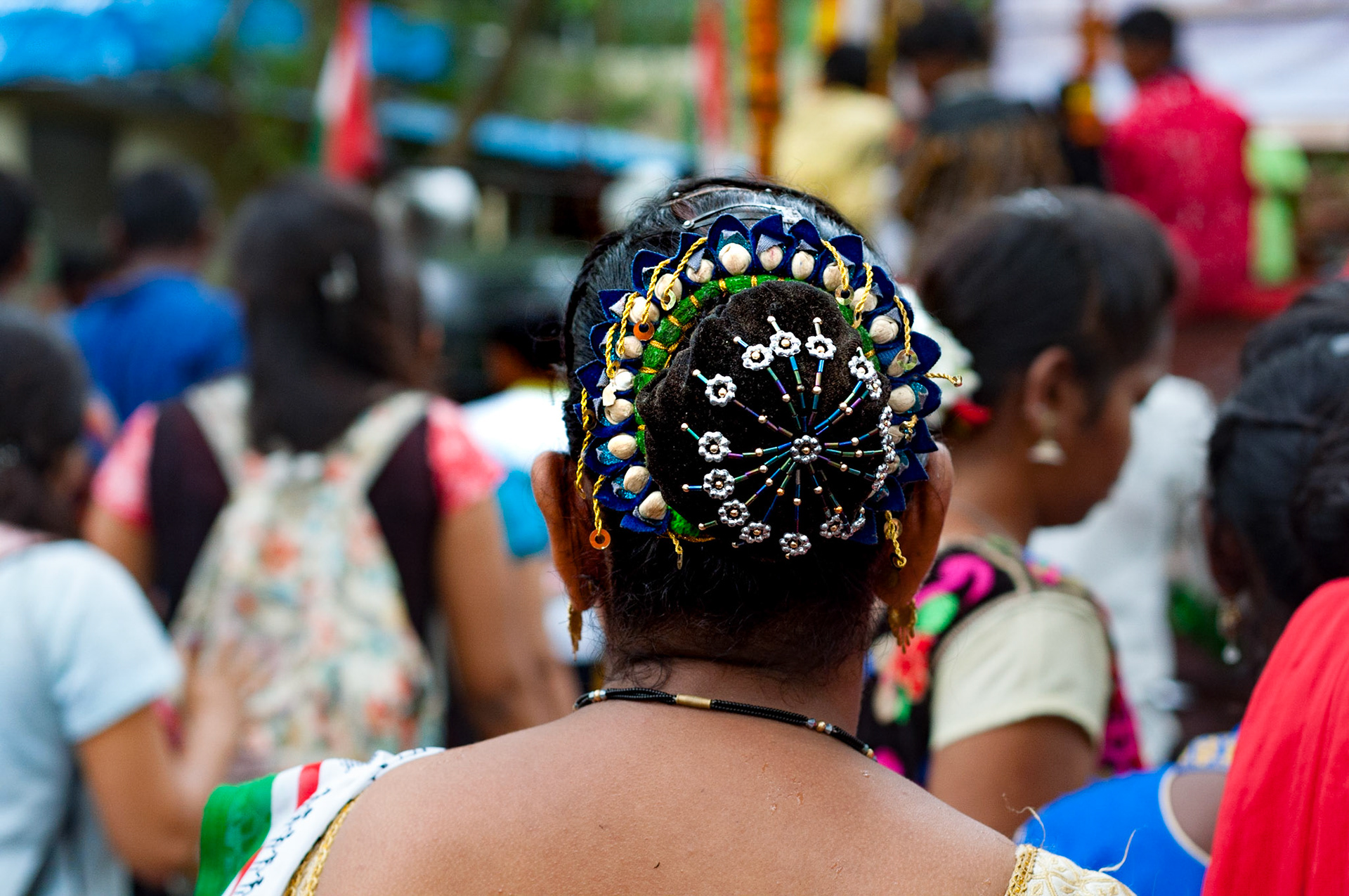 Colourful traditional hair decoration of Warli woman, shot from behind. People in soft focus background. The Warli are indigenous tribal people of Mumbai, northern Maharashtra and southern Gujarat, known for their distictive art style.