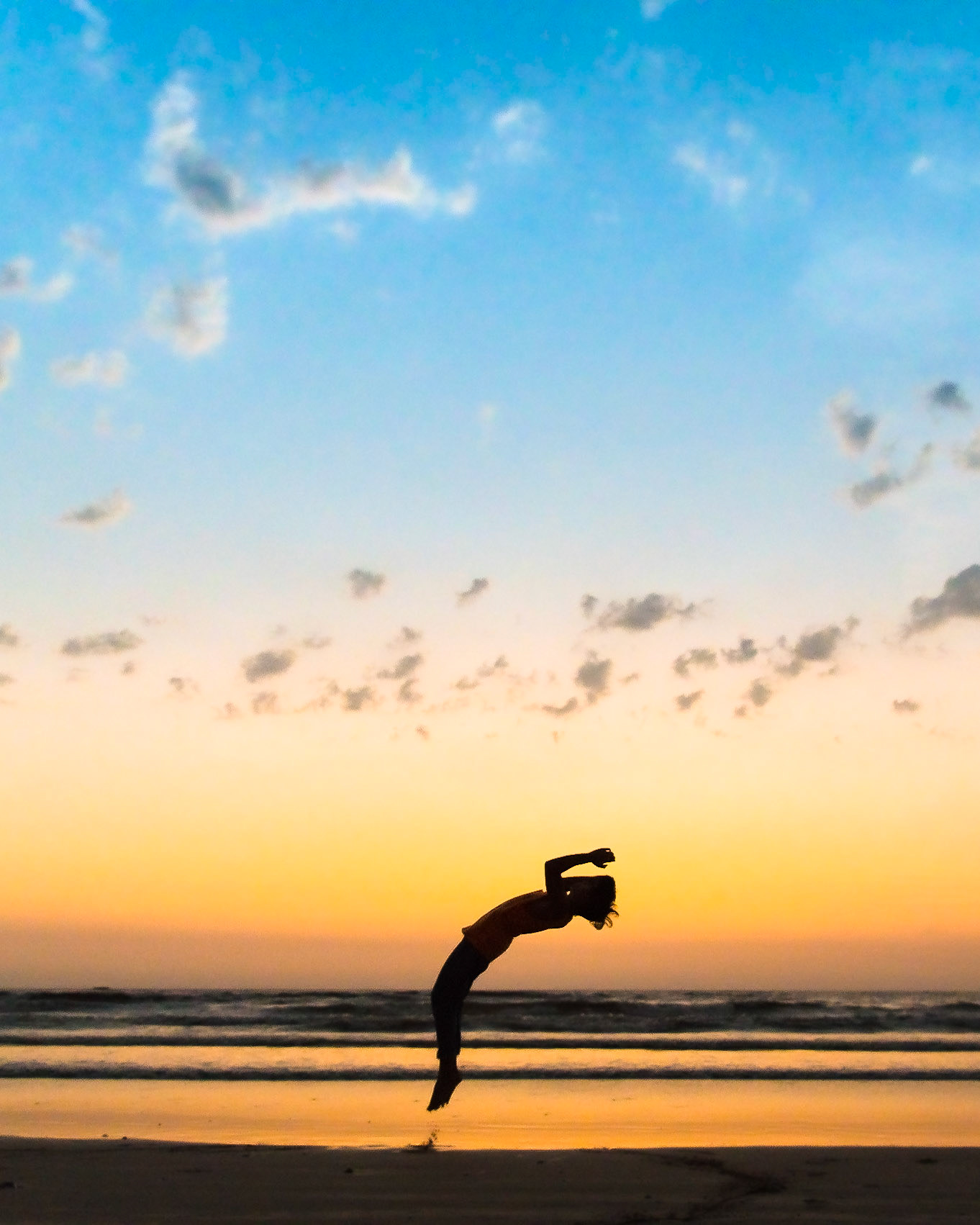 MUMBAI, INDIA – March 14 2019: On a hot summer evening youth performs somersaults, flips and handstands at the beach. Silhouetted at dusk with clouds in the sky.