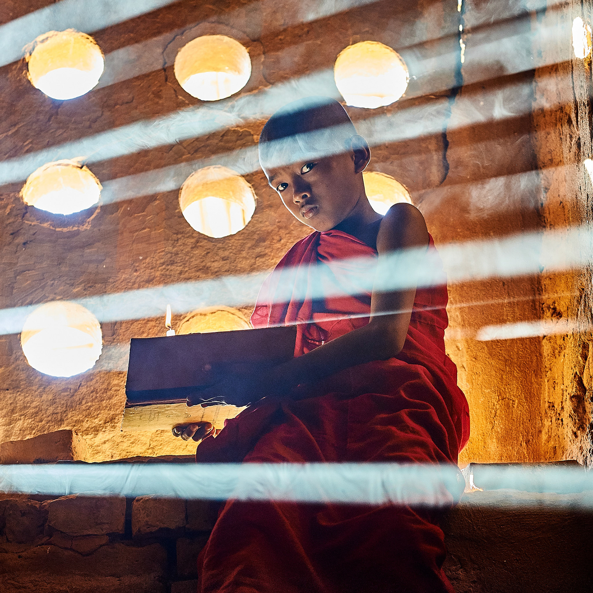 A young Buddhist monk in Bagan (Myanmar) sitting in rays of sunshine