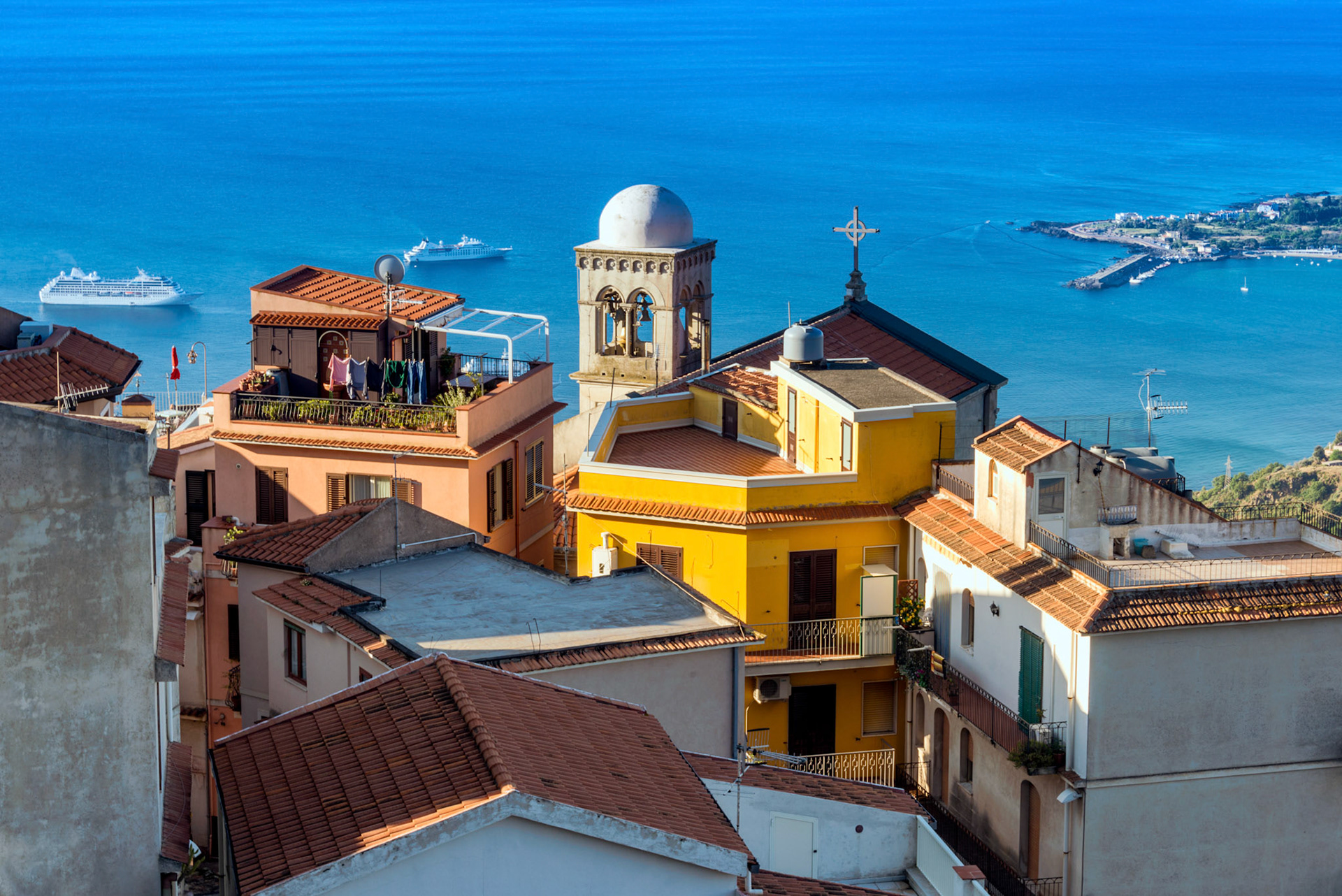 View from Castelmola, Sicily: the bell tower in the light of the morning sun and 2 cruise ships in the sea.
