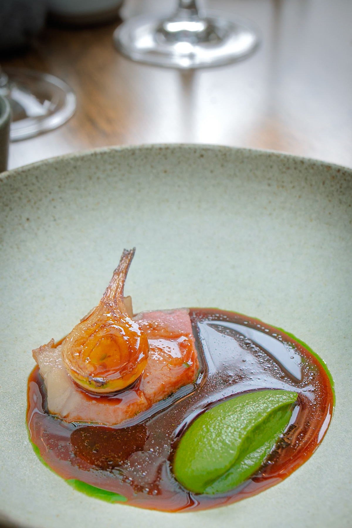 L'Enclume | Texel Cross lamb loin, roasted on the bone with barbecue Piroska onion marinated in our own shio koji, green onion purée, ramson leaves and chive flowers and a sauce made from the lamb bones spiked with fig leaf vinegar.
