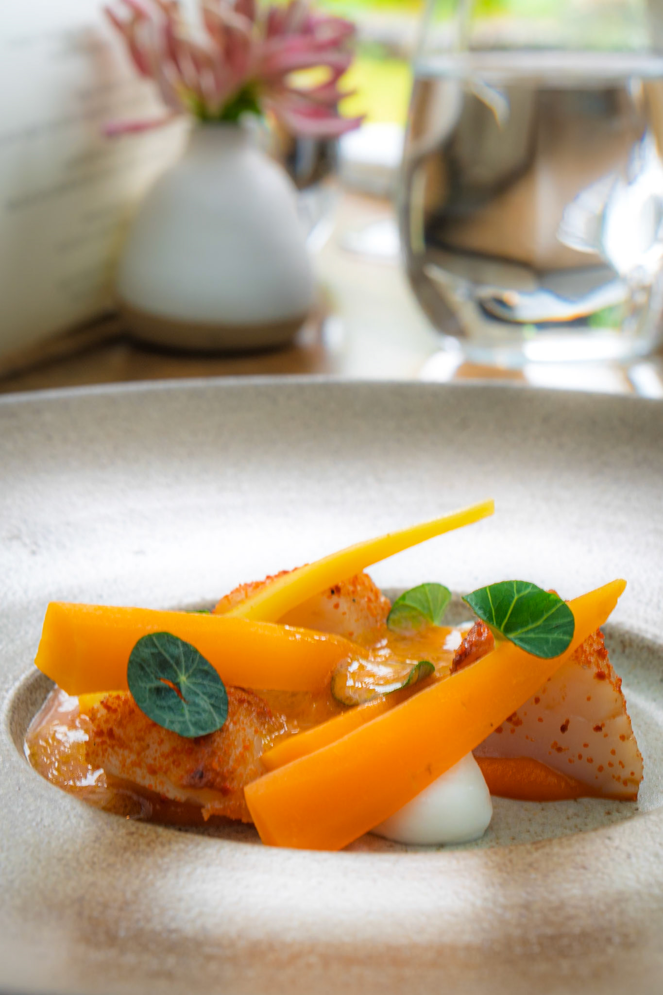 L'Enclume | Lisse de meaux carrots cooked in rapeseed infused with nasturtium stems, with raw slices dusted in nasturtium powder and puree. Scallops from Orkney that have been brined and glazed with scallop garum and dried roe powder; ham fat emulsion, nasturtium leaves and a dressing made from nasturtium flowers, black garlic oil and our verjus.