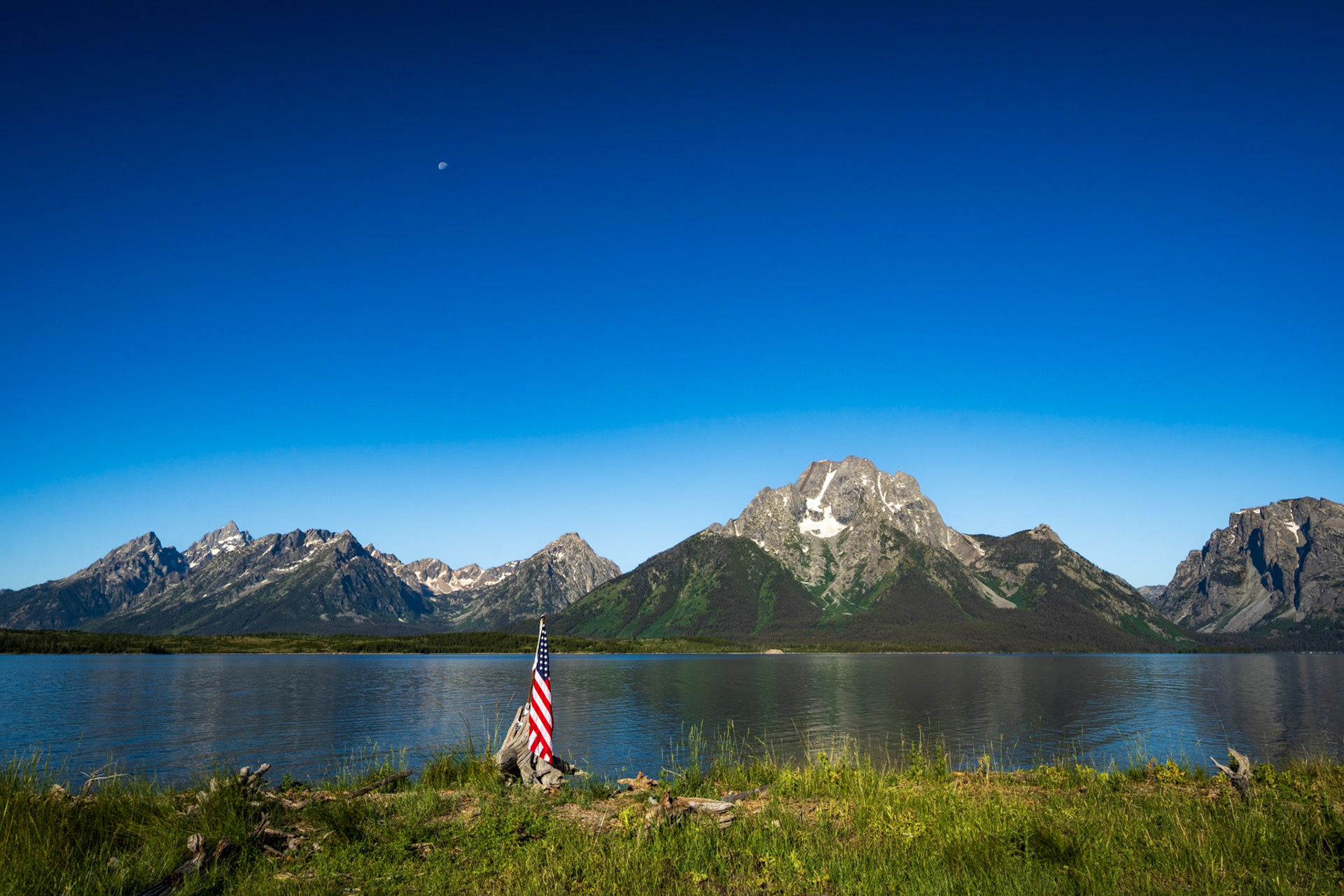An American flag on the shoreline of Jackson Lake in front of the Teton mountain range. Grand Teton National Park