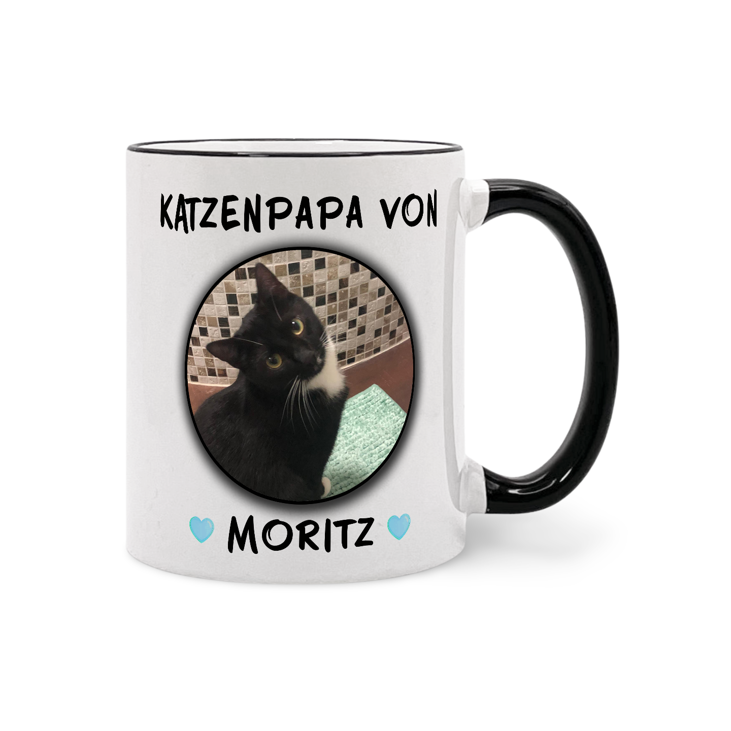 Weiße Tasse mit schwarzem Henkel und Aufdruck eines schwarz-weißen Katzenporträts mit dem Text 'KATZENPAPA VON MORITZ' und zwei kleinen blauen Herzen