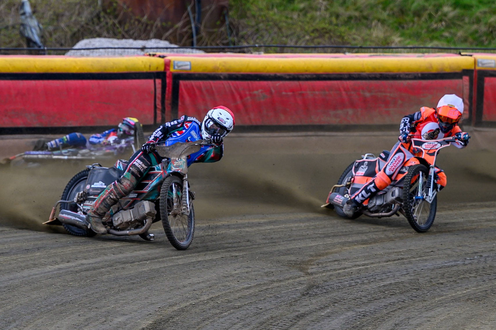 Alfie Bowtell of Buxton Bulls  in Red Connor Coles of NDL Nomads in White as Sam Woods of NDL Nomads  slides into the safety fence during the  Challenge match between Buxton Bulls and NDL Nomads at Hi-Edge Speedway, Buxton on Sunday 19th April 2026. (Photo: Ian Charles | MI News)