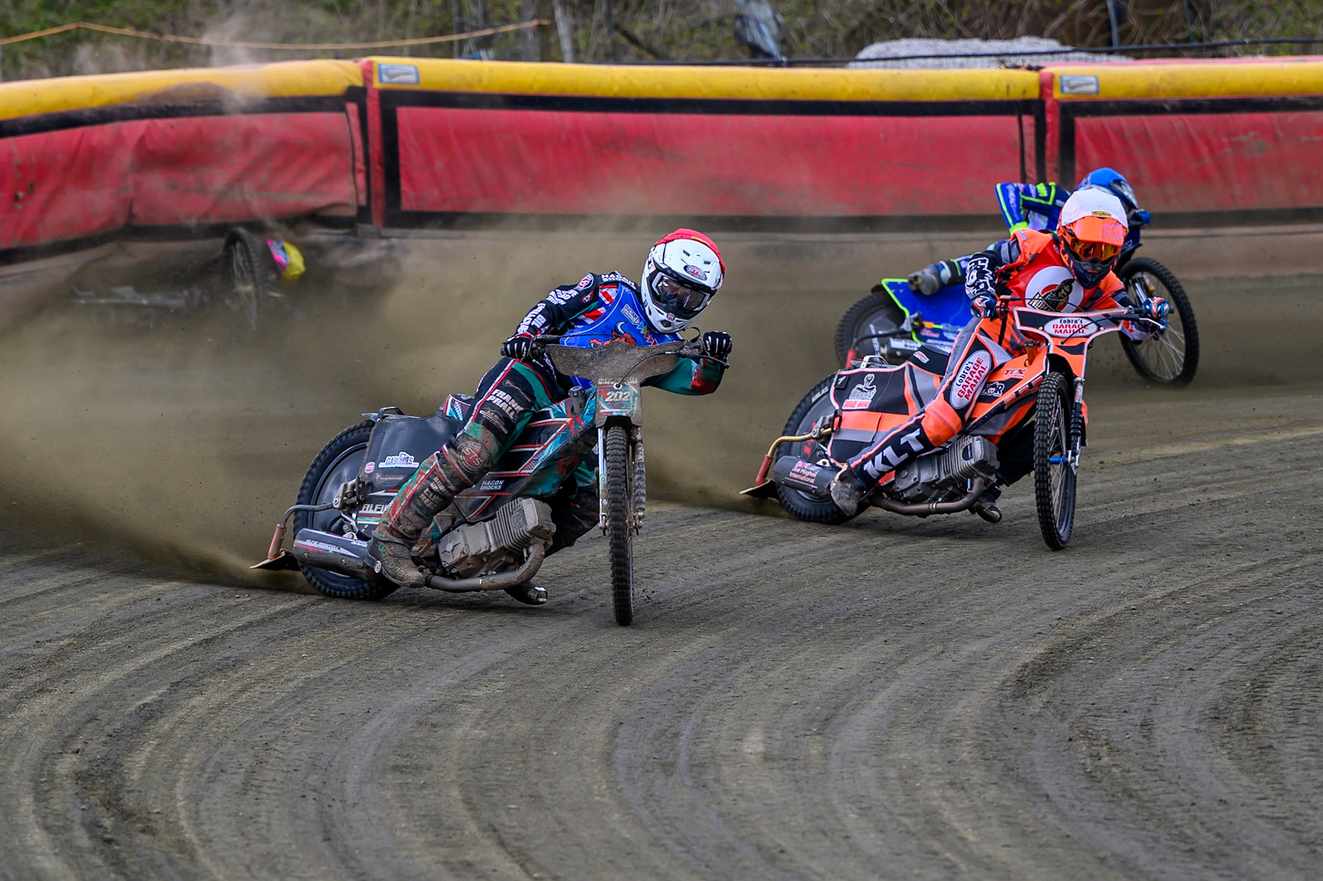 Alfie Bowtell of Buxton Bulls  in Red Connor Coles of NDL Nomads in White as Sam Woods of NDL Nomads  slides into the safety fence as Arran Butcher of Buxton Bulls  spins his machine during the  Challenge match between Buxton Bulls and NDL Nomads at Hi-Edge Speedway, Buxton on Sunday 19th April 2026. (Photo: Ian Charles | MI News)