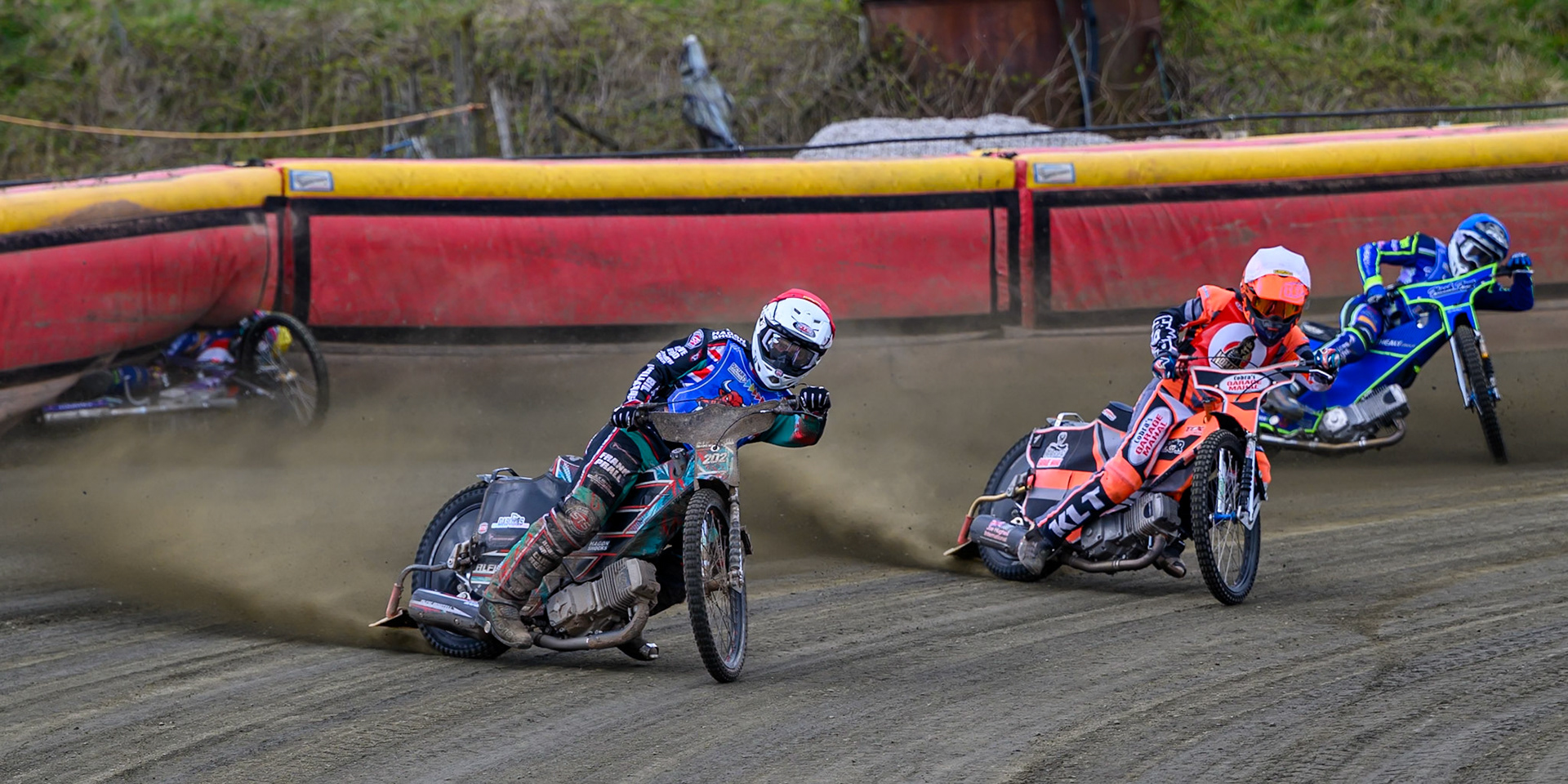 Alfie Bowtell of Buxton Bulls  in Red Connor Coles of NDL Nomads in White as Sam Woods of NDL Nomads  slides into the safety fence as Arran Butcher of Buxton Bulls  spins his machine during the  Challenge match between Buxton Bulls and NDL Nomads at Hi-Edge Speedway, Buxton on Sunday 19th April 2026. (Photo: Ian Charles | MI News)